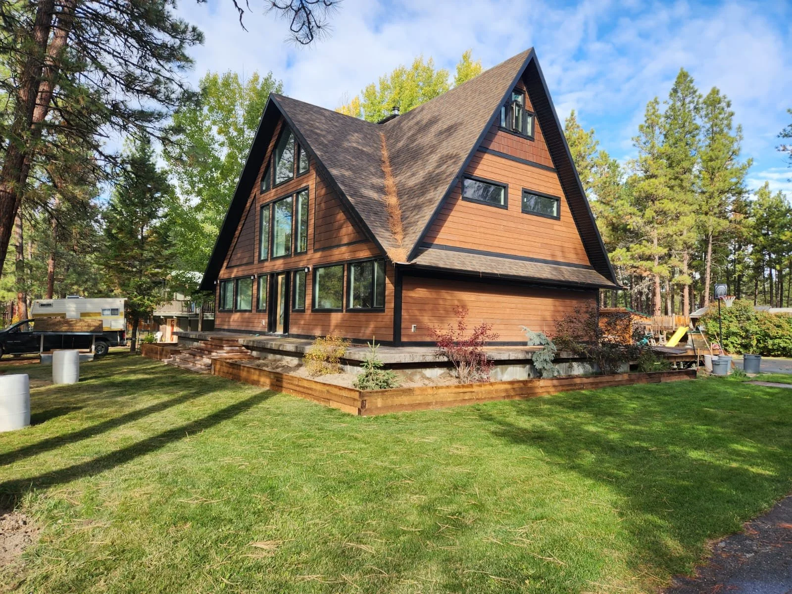 A modern wooden house with steep gabled roof surrounded by green trees and a well-maintained lawn.