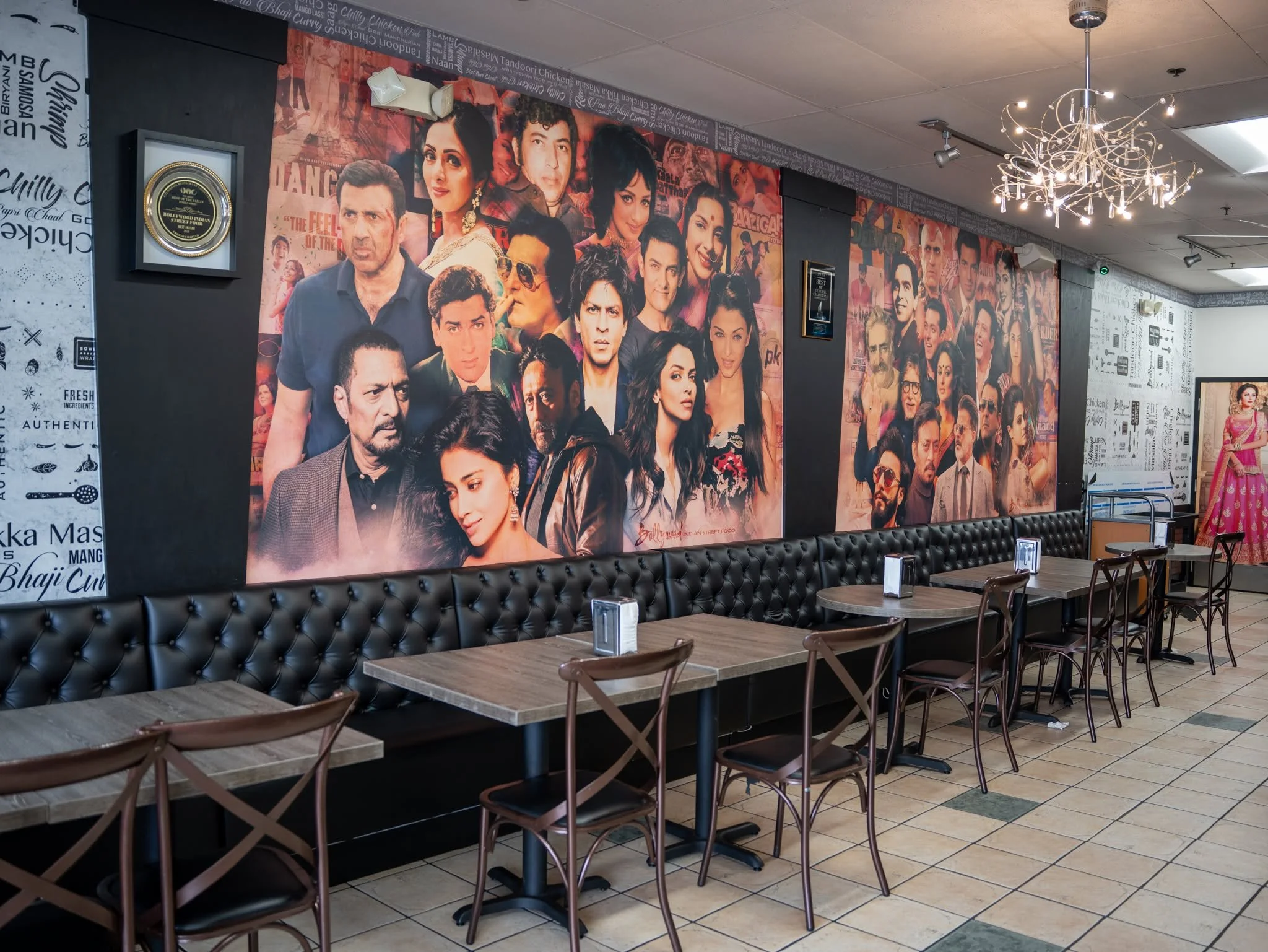Interior of a restaurant featuring large collage posters of Bollywood actors on the wall, with tables and chairs arranged in front.