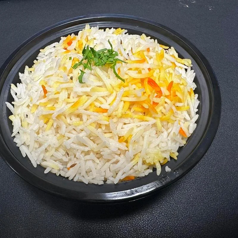 A bowl of cooked rice with shredded cheese and a small garnish of chopped herbs on top, sitting on a dark surface.