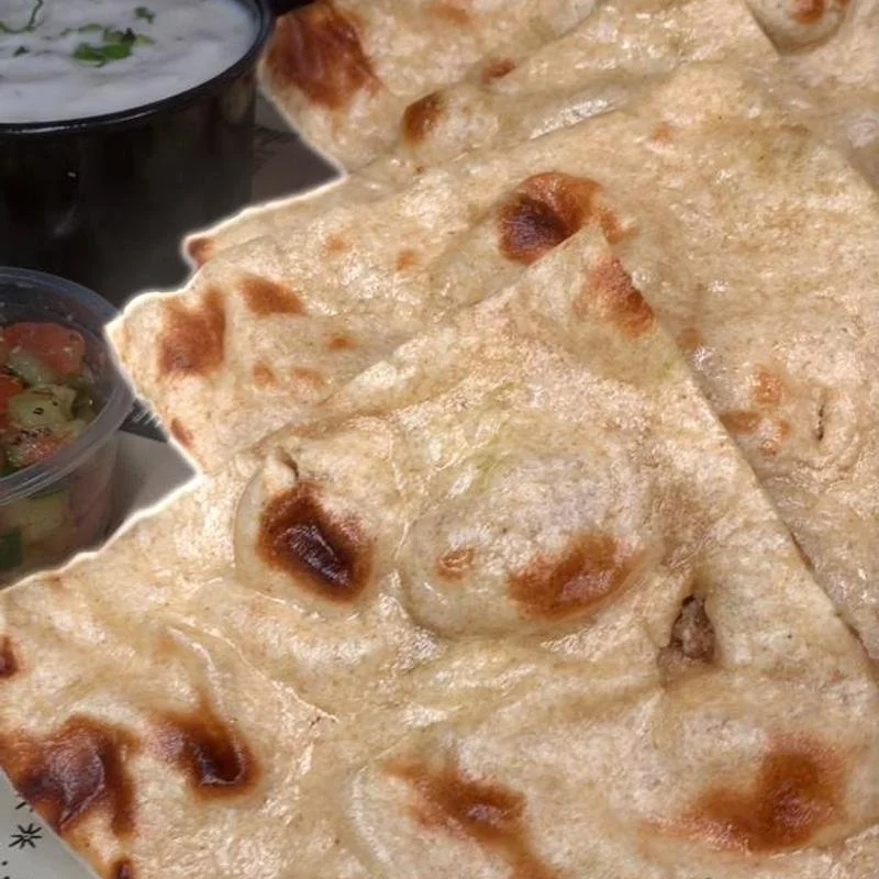 Close-up of naan bread with golden-brown spots, accompanied by small bowls of cucumber raita and salad.