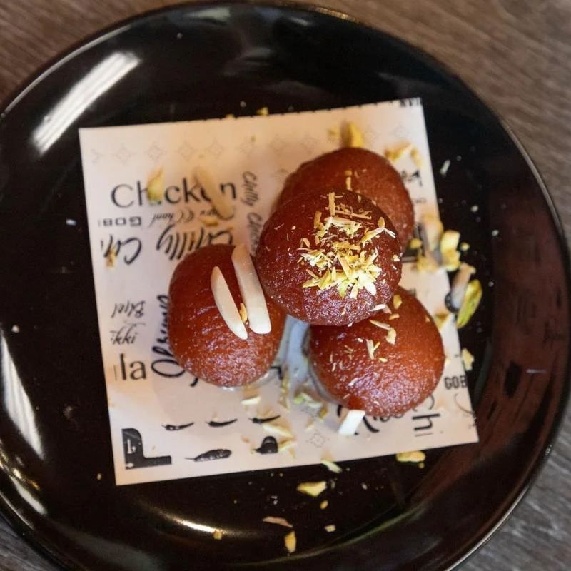 Plate with four small round chocolate cake balls topped with white chocolate shavings, on a piece of printed paper on a black plate.