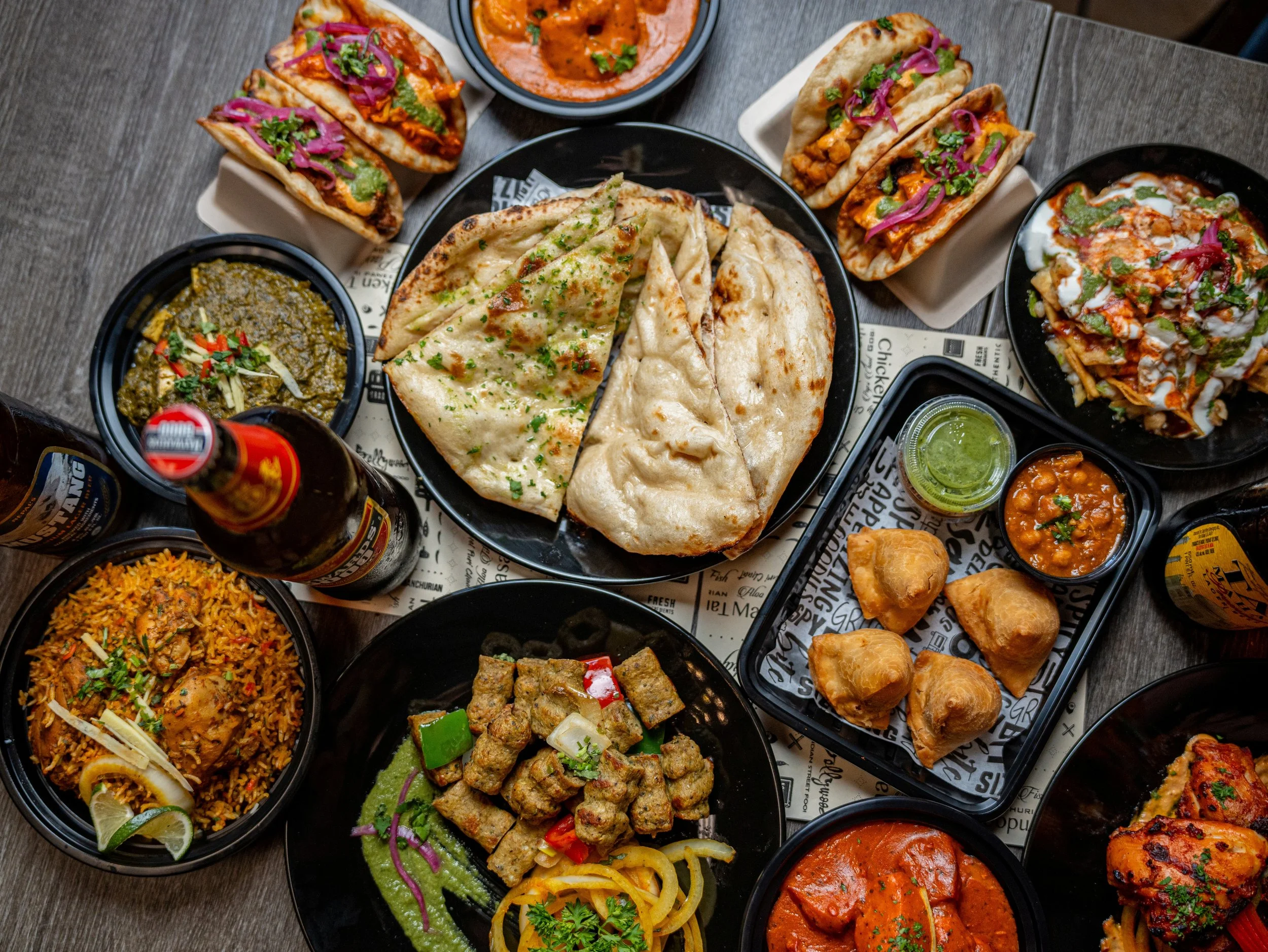 Assorted Indian dishes including naan bread, curries, rice, and appetizers on a dark table.