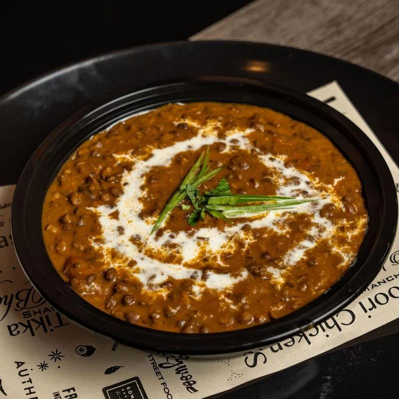 A bowl of Indian lentil curry garnished with fresh green herbs and a swirl of cream, served on a black tray.
