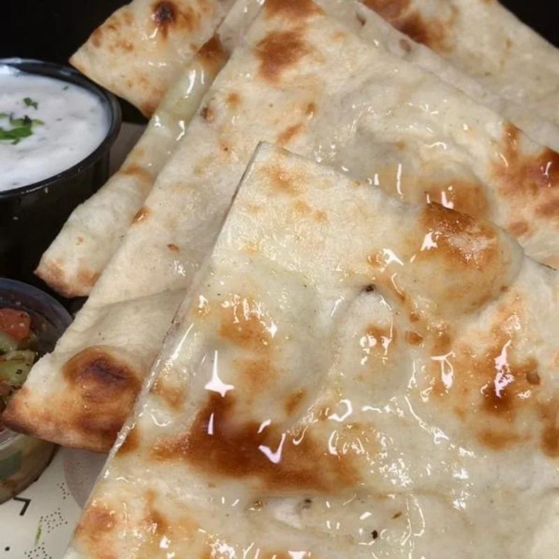 Close-up of a cheese pizza with a thin crust, topped with melted cheese, and a side of creamy dipping sauce