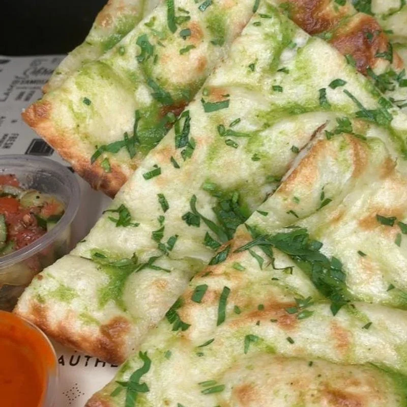 Close-up of cheese garlic bread topped with chopped parsley, served with small containers of side salads.