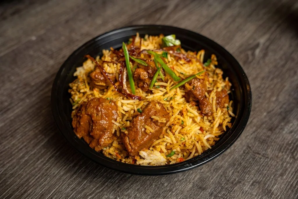 A black bowl filled with rice and chunks of beef stew, garnished with chopped green onions, on a wooden surface.