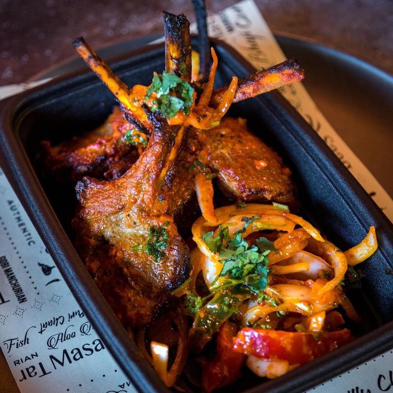 Close-up of grilled lamb chops with roasted vegetables and herbs in a black container