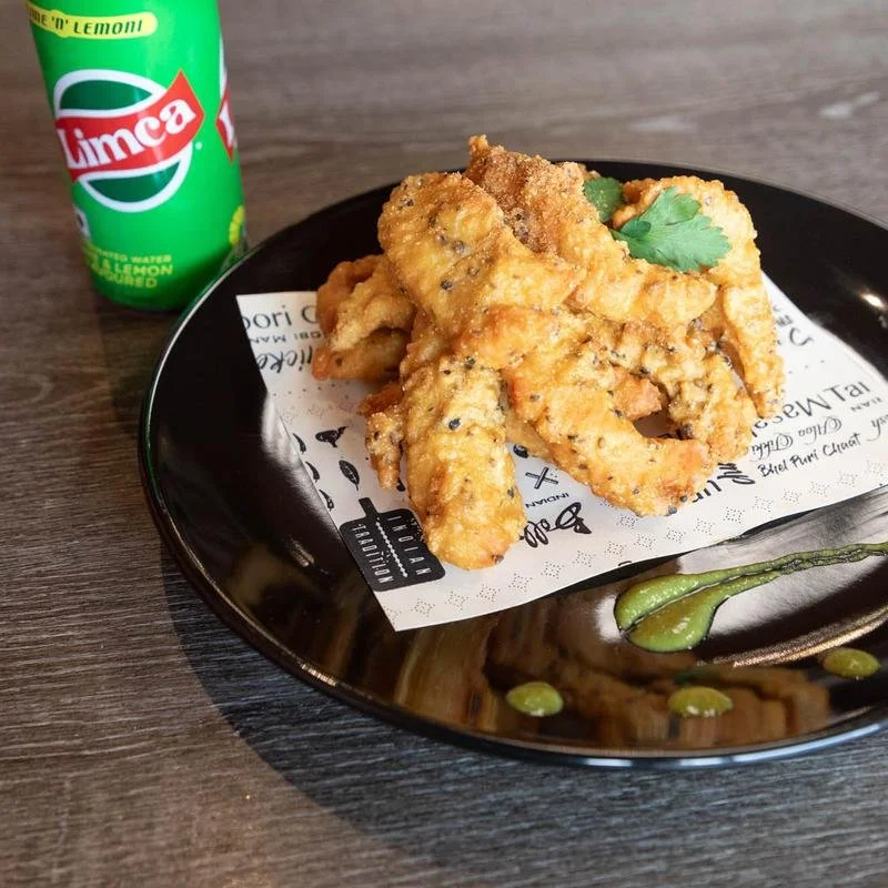Fried fish fillets on a black plate garnished with a cilantro leaf, with a green Sprite lime soda can in the background.