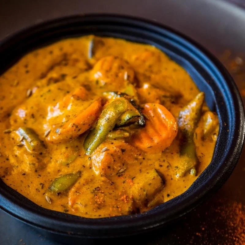 A bowl of Indian curry with vegetables such as carrots and green beans in a thick, yellowish sauce.