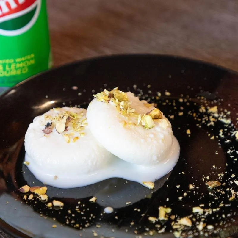 Two soft-boiled eggs topped with chopped pistachios on a black plate.