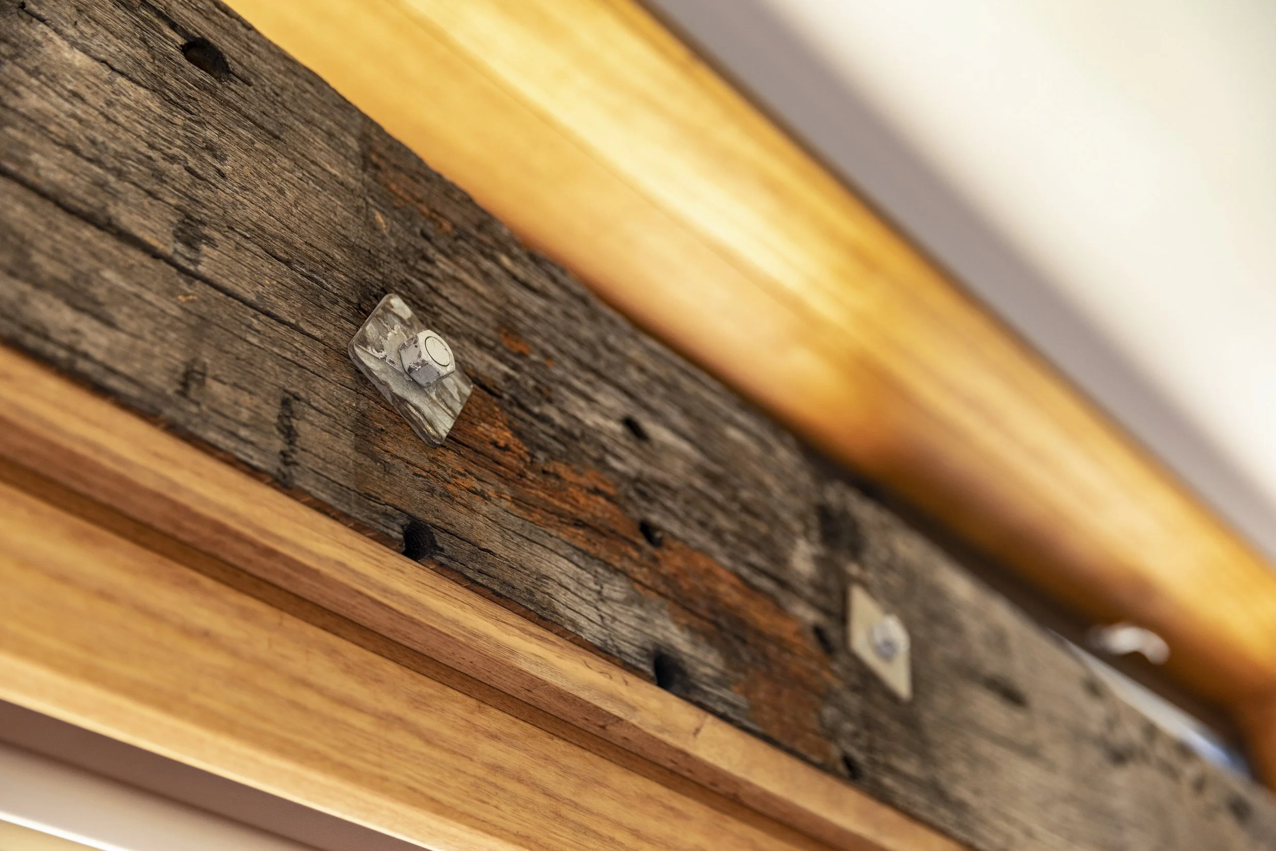 Close-up of a section of a wooden wall with a metal bracket attached, showing a combination of weathered and new wood panels.