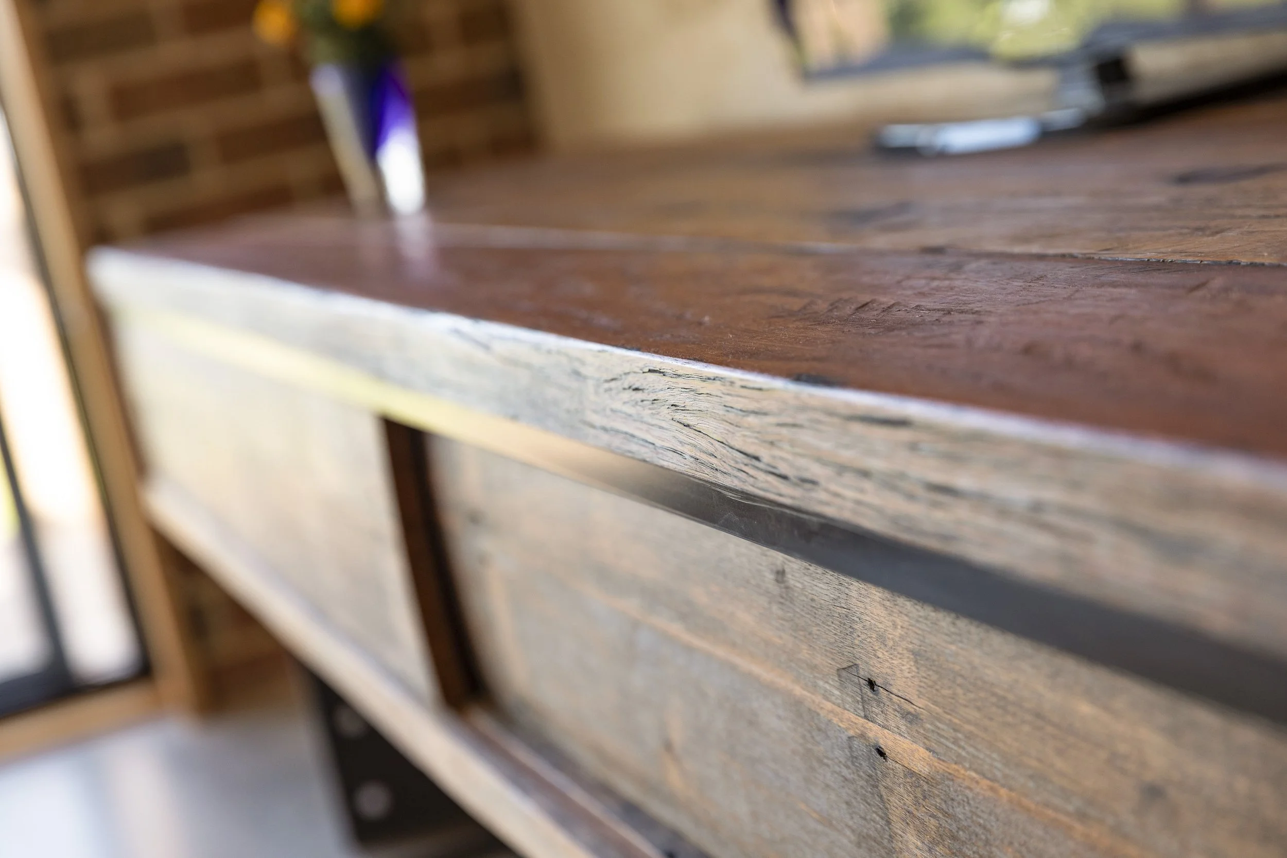 Close-up of a wooden table surface with visible grain and texture, showing a slightly rough and weathered finish.