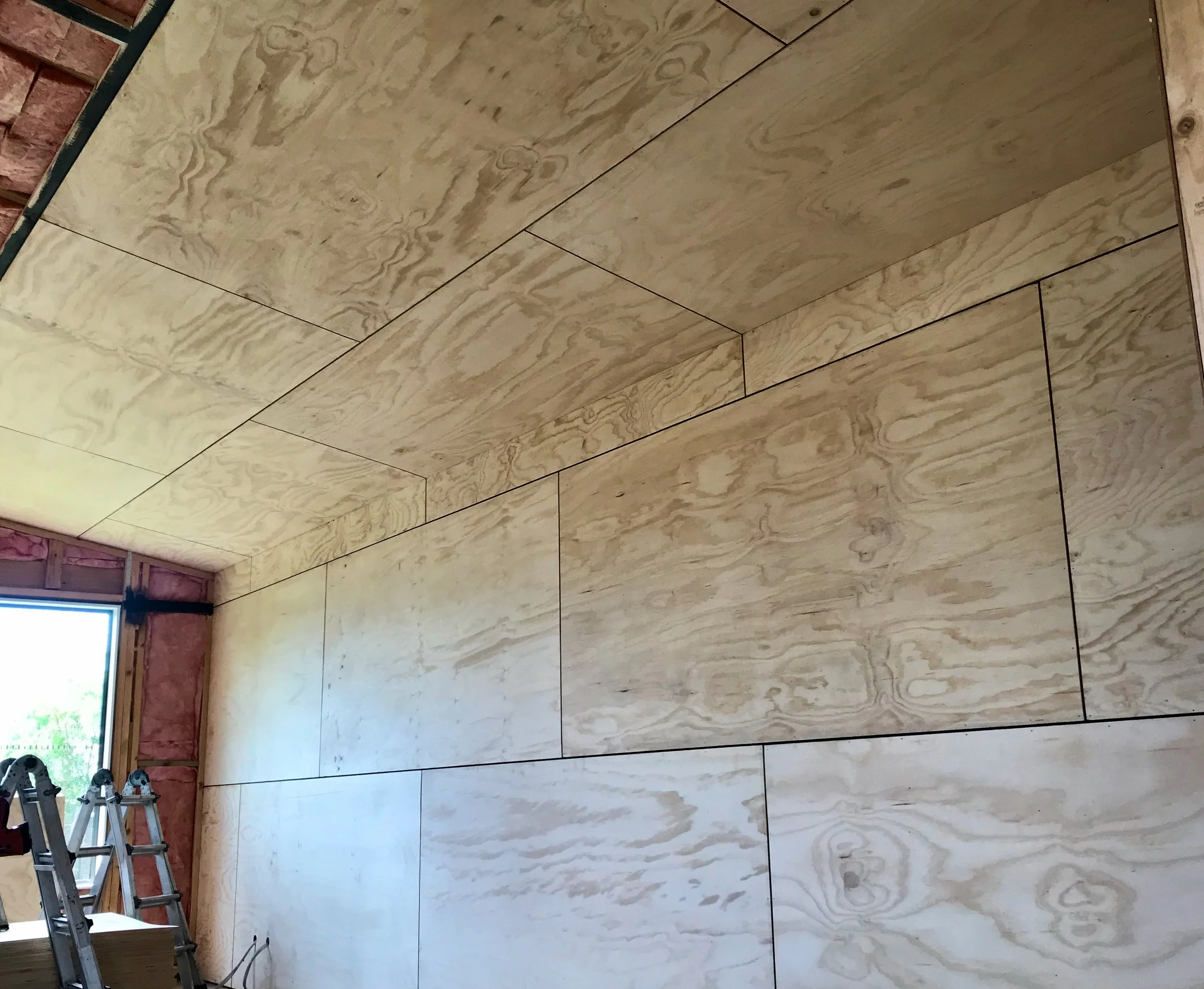 Interior of a room under construction with unfinished wooden walls and an open window in the corner.