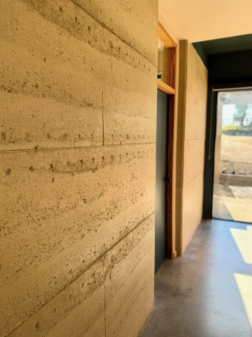 Interior space with beige textured walls, a wooden-framed doorway, and a glass door leading outside to a yard with a slight slope.