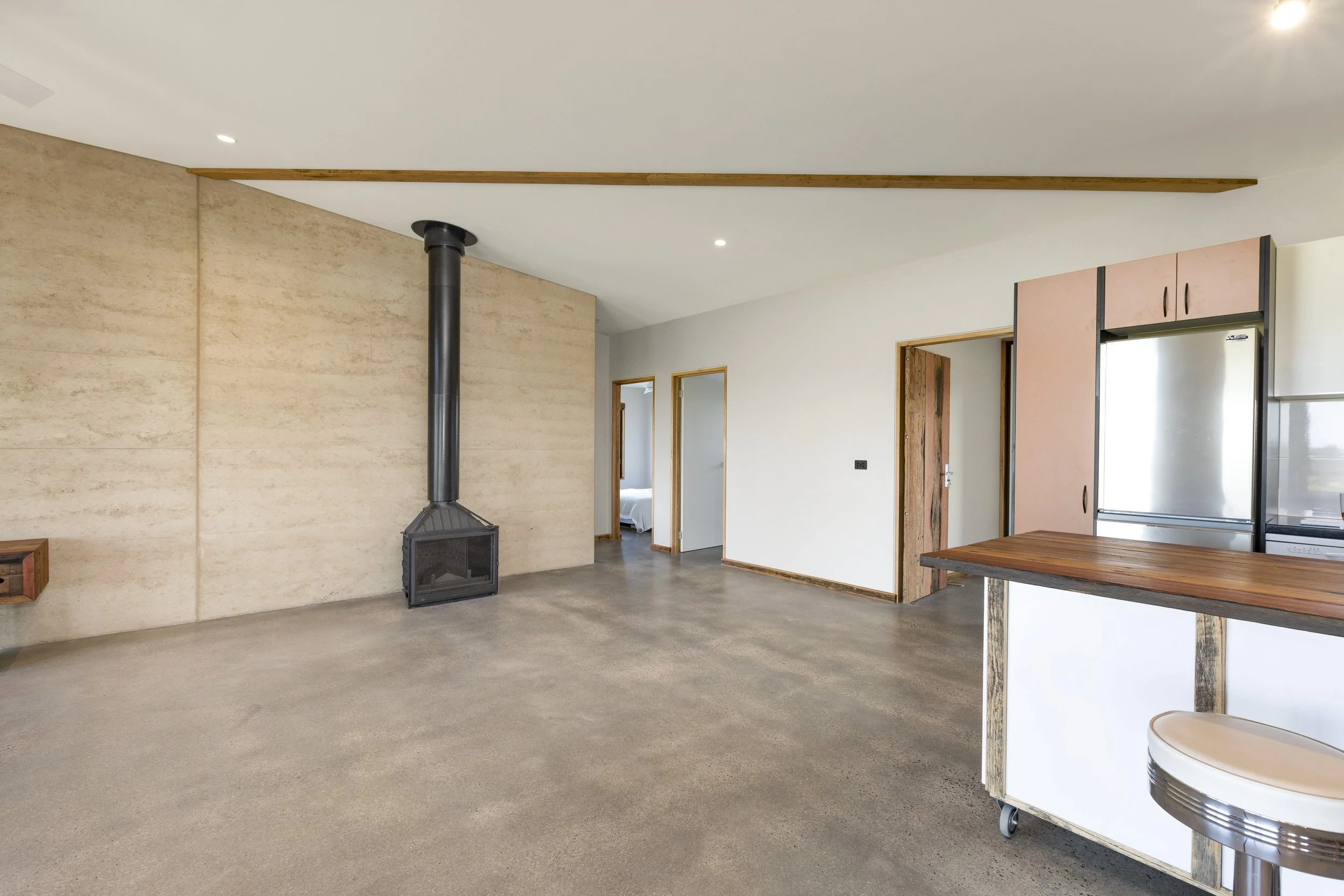 Open-concept living space with polished concrete floors, a wood-burning stove, and natural wood accents on doors and ceiling beams.