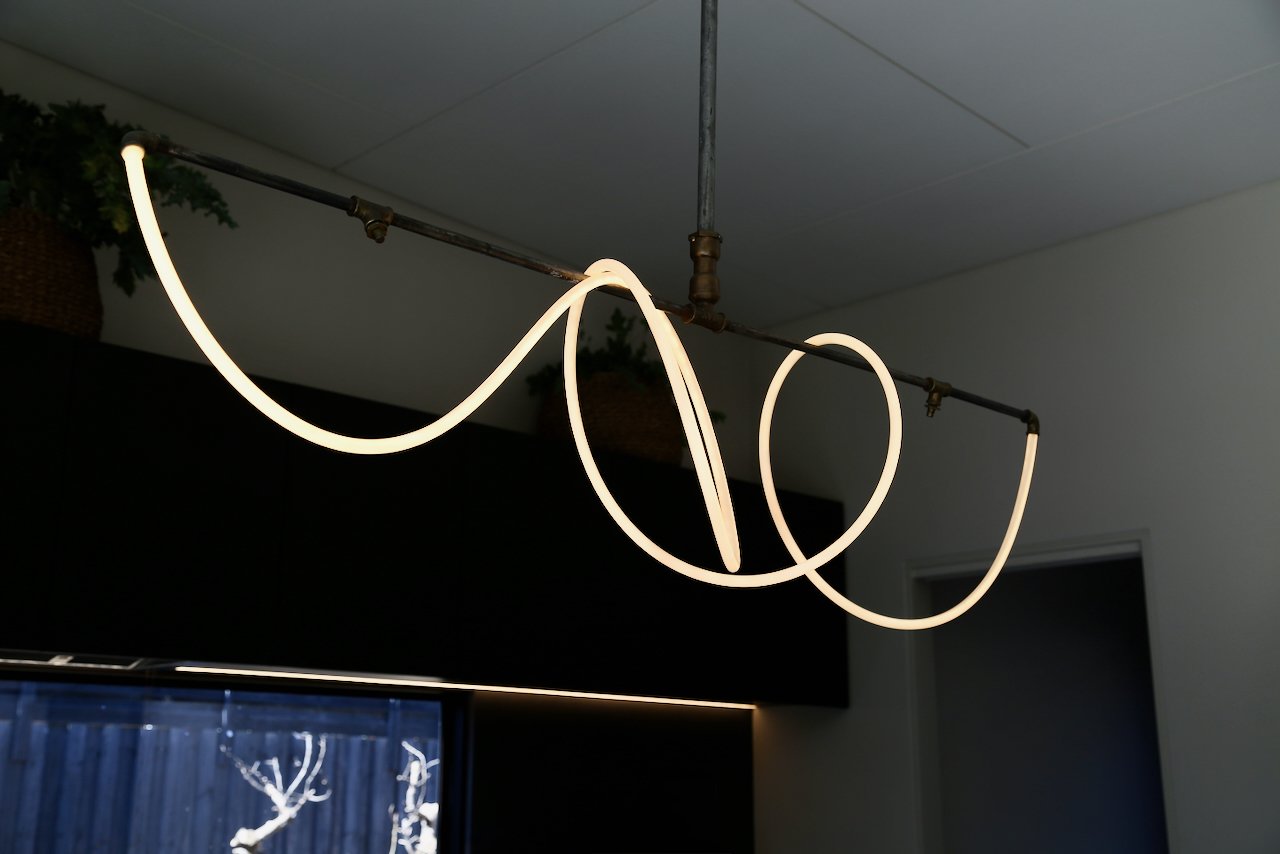 Modern ceiling light fixture with an LED strip arranged in a flowing, abstract pattern, hanging from a dark ceiling.