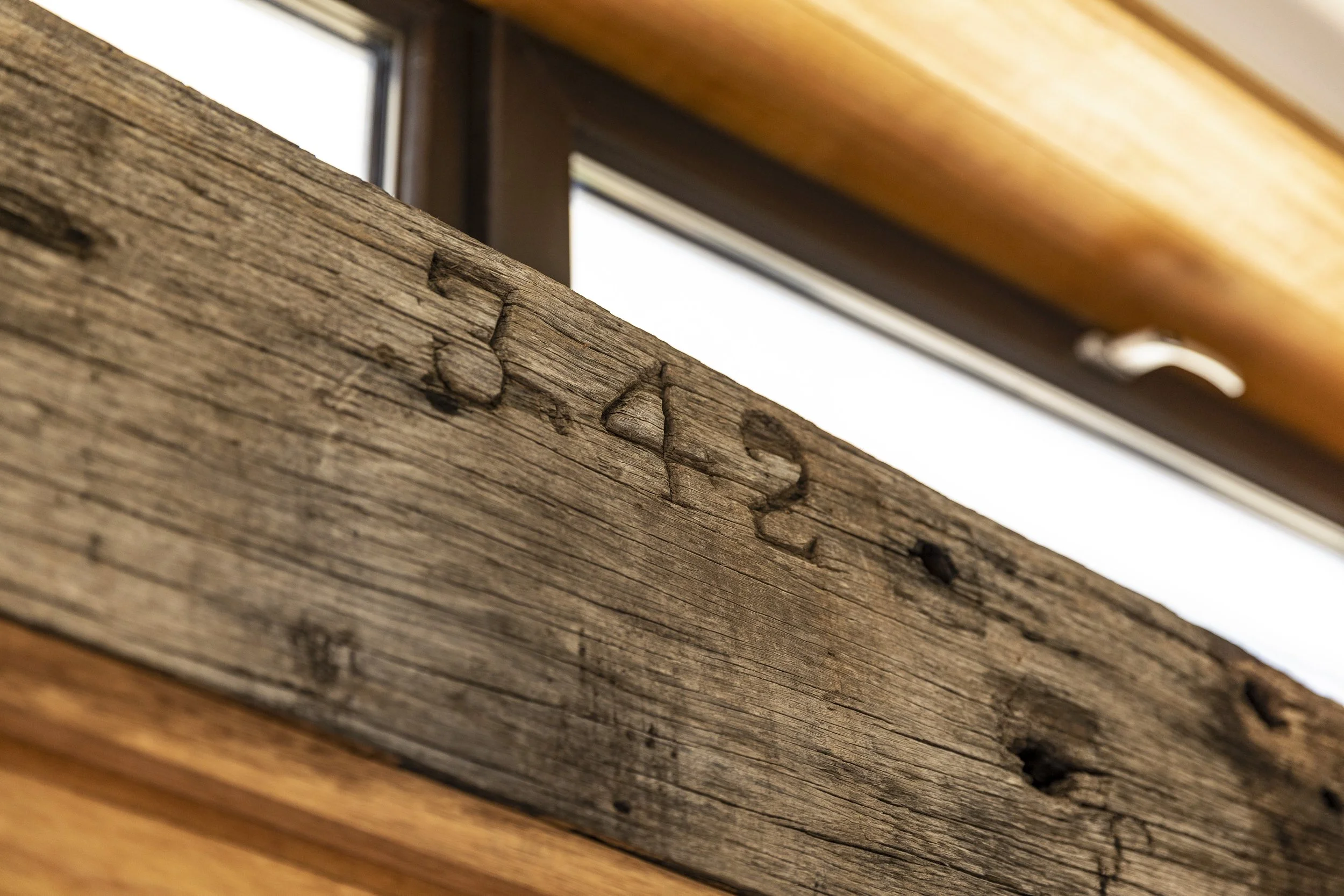 Close-up of weathered, textured wooden surface with visible grain and nail holes near a window and a wood-paneled ceiling.