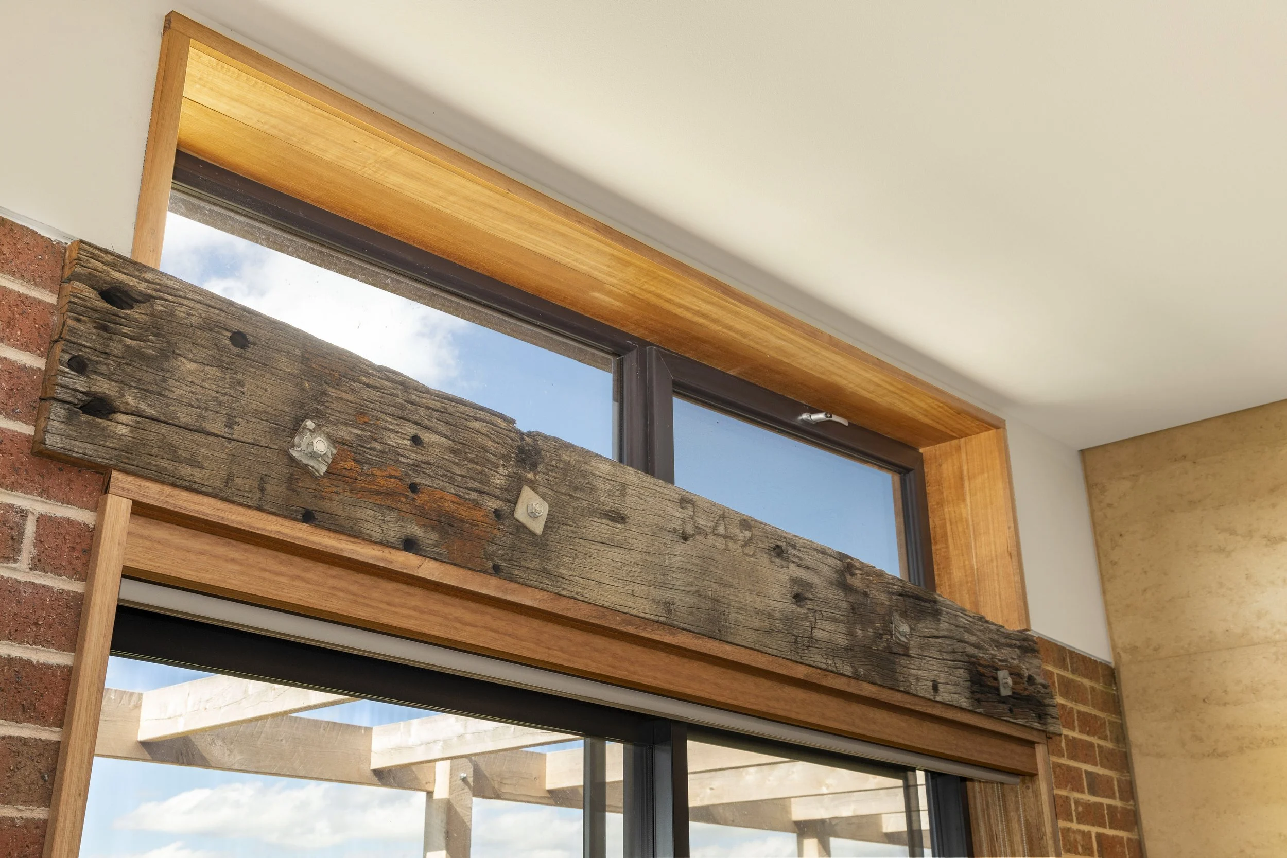View from inside of a room showing a wooden beam, a window with a sky and clouds outside, and brick and wooden interior walls.