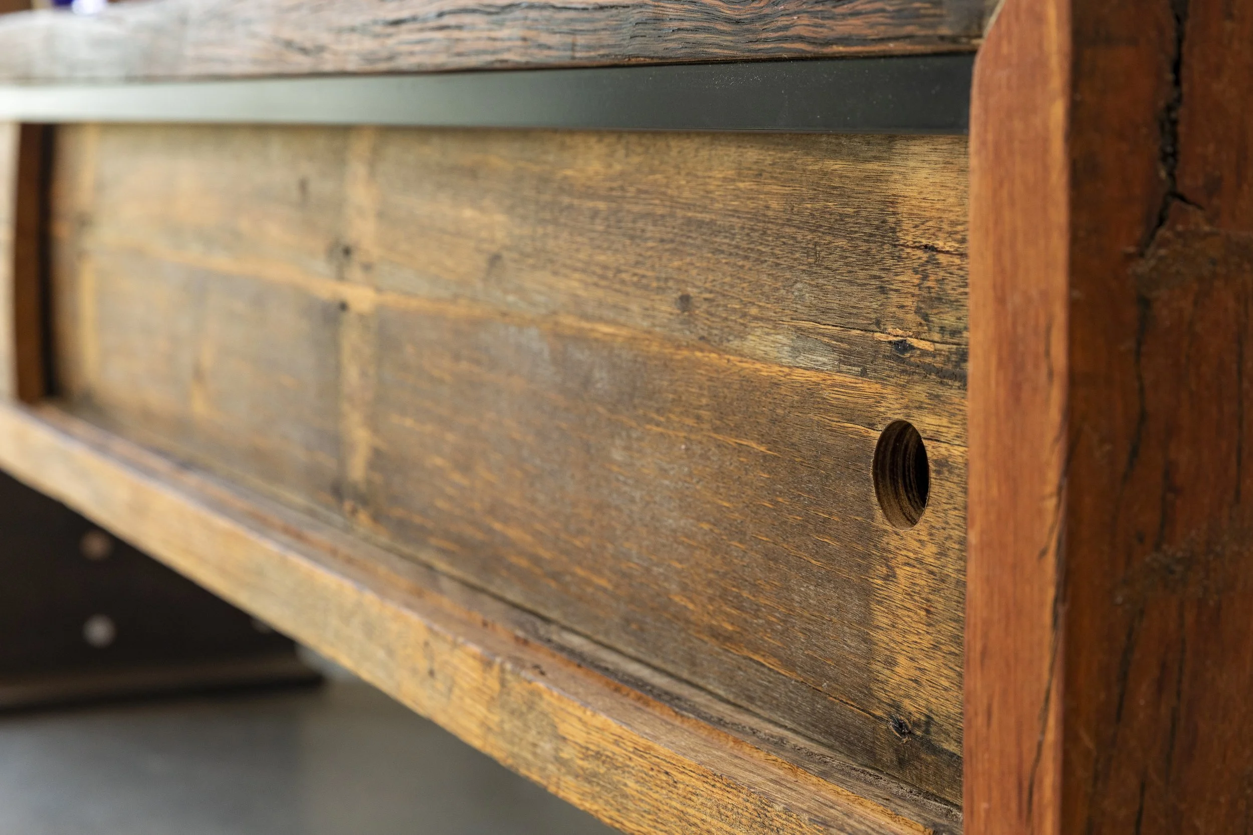 Close-up of a wooden surface with a round hole, showing textured grains and a combination of dark and light wood tones.