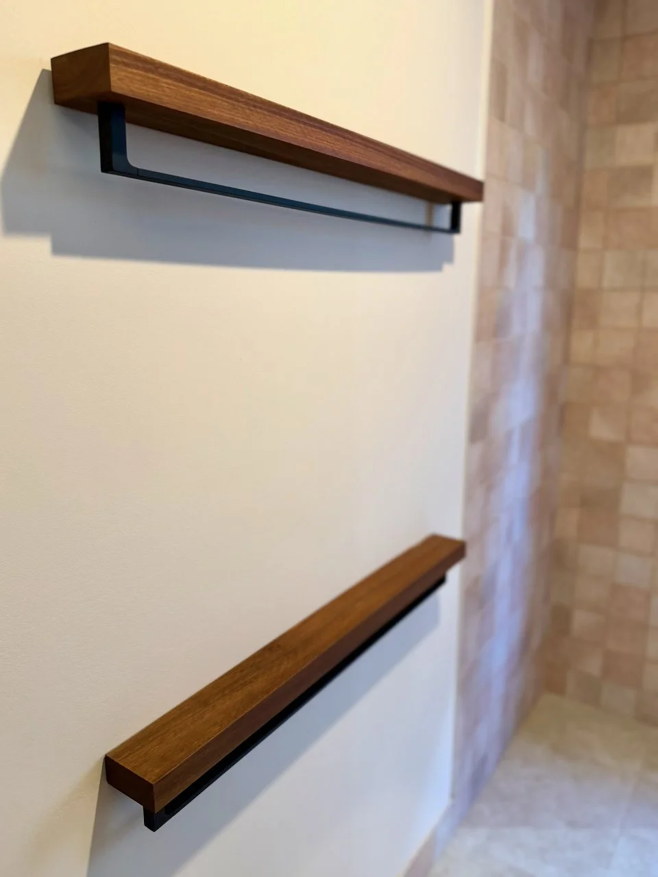 Two wooden and metal handrails mounted on a wall, with a beige wall on the left and a brick wall on the right.