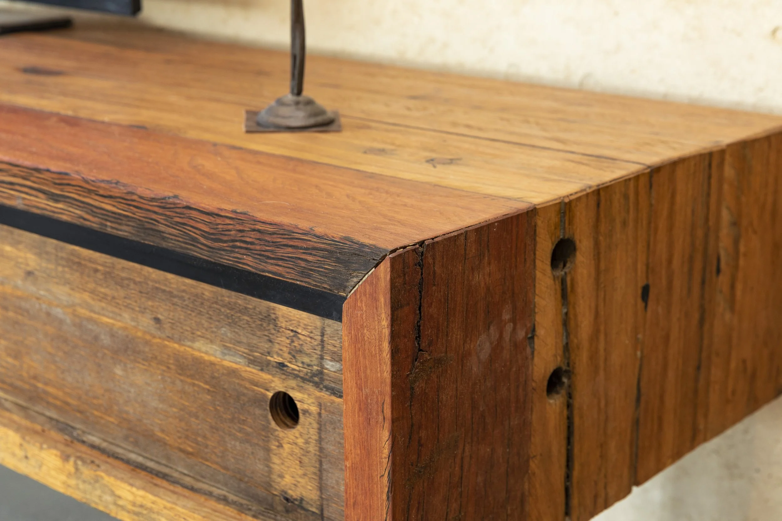 Close-up of a wooden furniture piece with a focus on the corner, showing the natural grain and texture of the wood, with some visible cracks and holes in the wood.