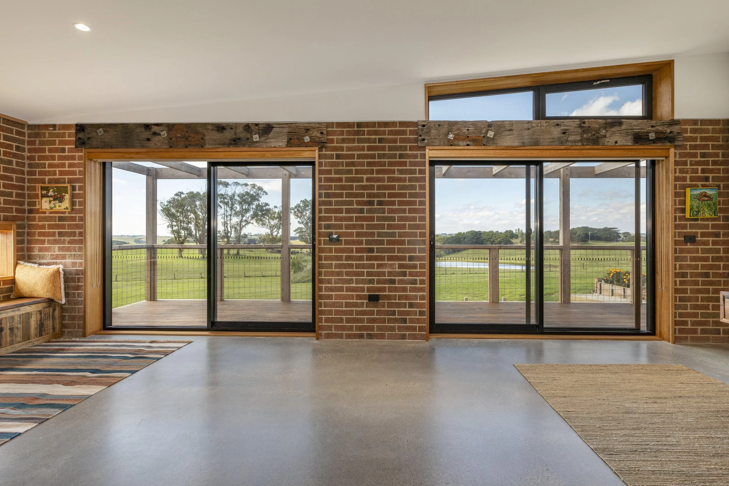 Interior of a room with large sliding glass doors leading to a deck and open fields outside, brick walls, and wooden accents.