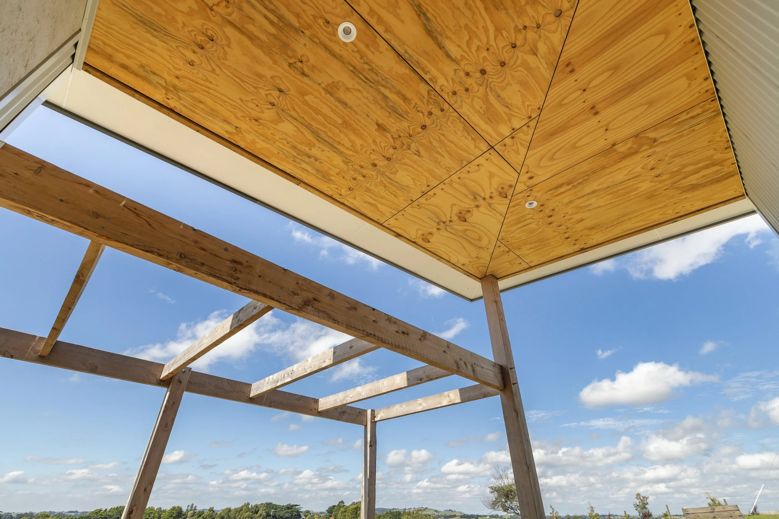 Construction of a wooden structure with a plywood ceiling, beams, and a partially open sky view.