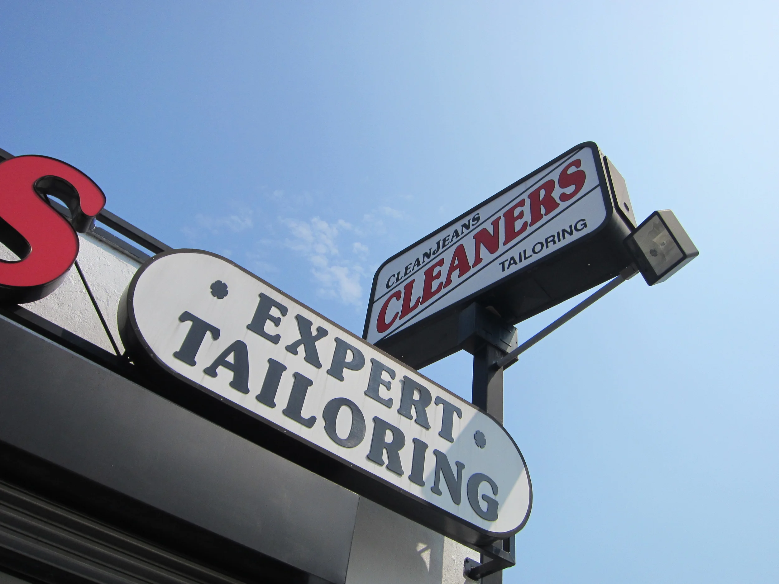 Signboards for a dry cleaning and tailoring business mounted outdoors against a blue sky.