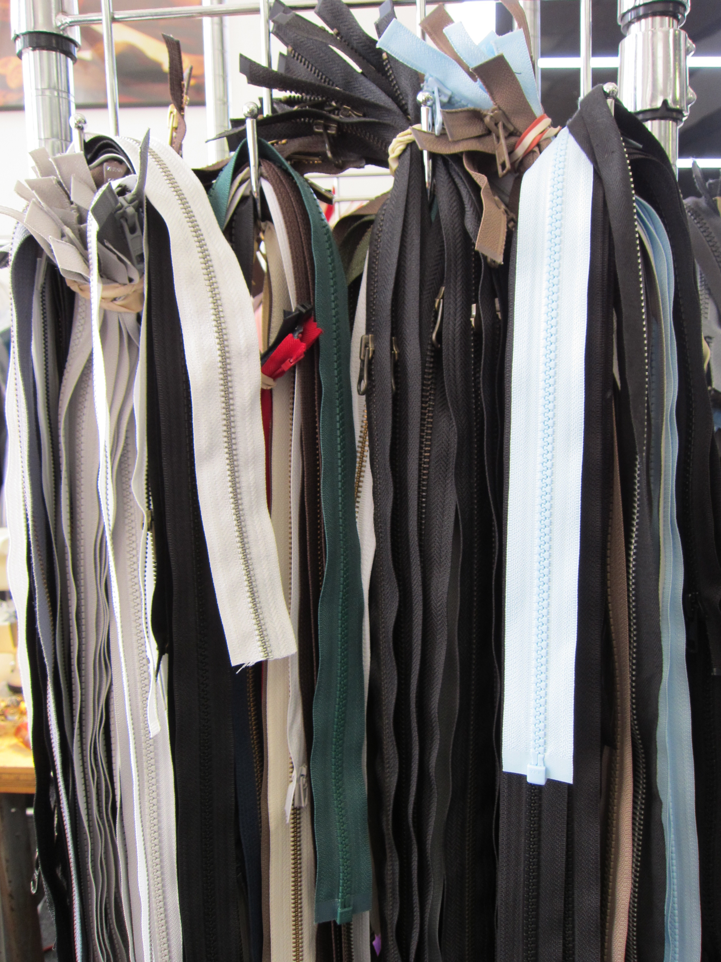 A display of various zippers in multiple colors and sizes hanging on metal hooks.