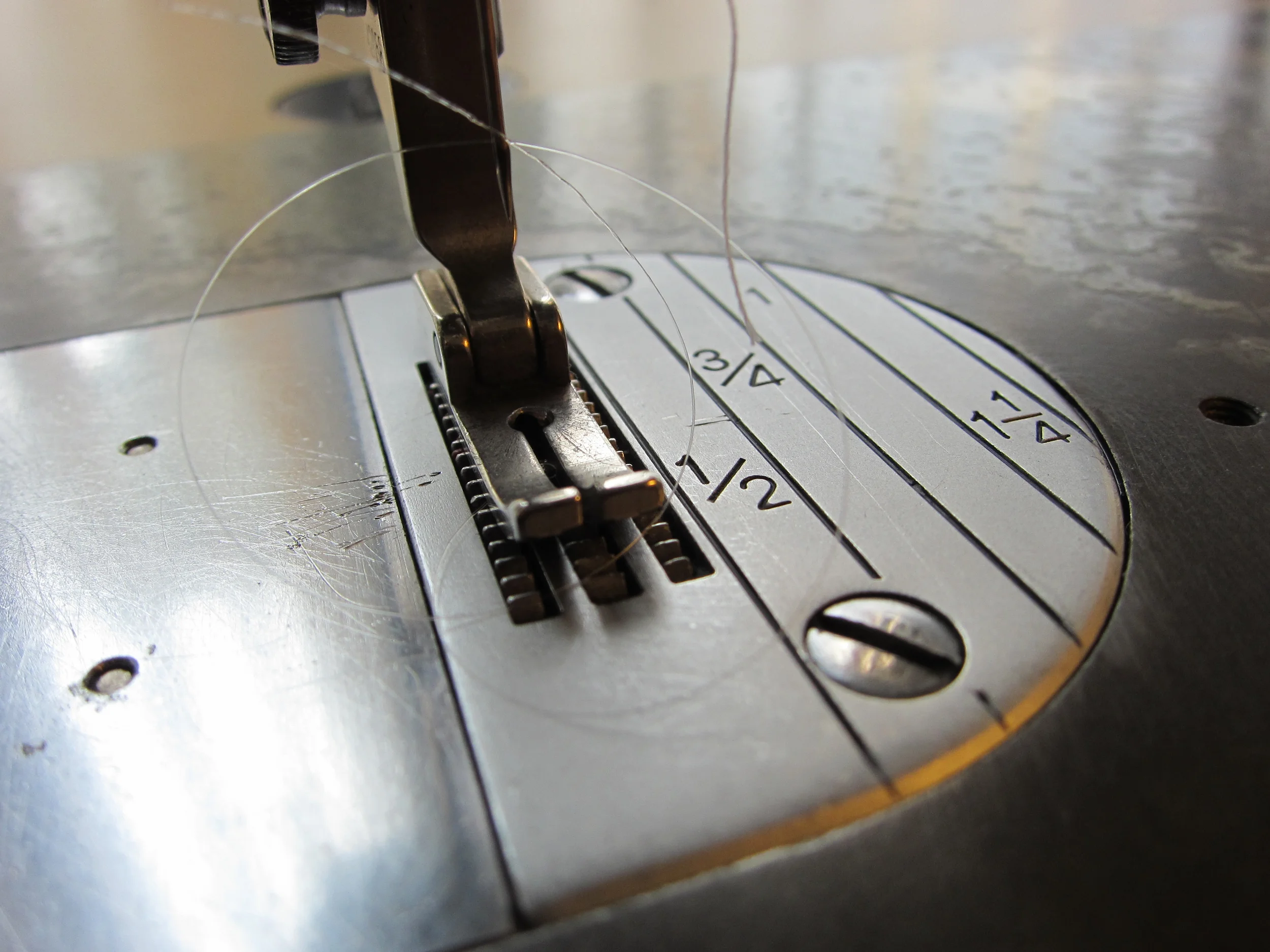Close-up view of a sewing machine needle and bobbin area, with the needle inserted into the fabric and thread visible.