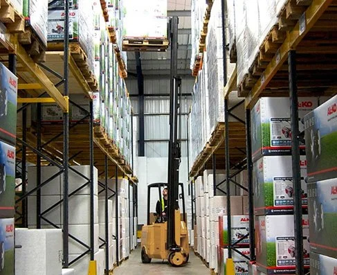 A yellow forklift moving between tall shelves filled with boxes in a warehouse.