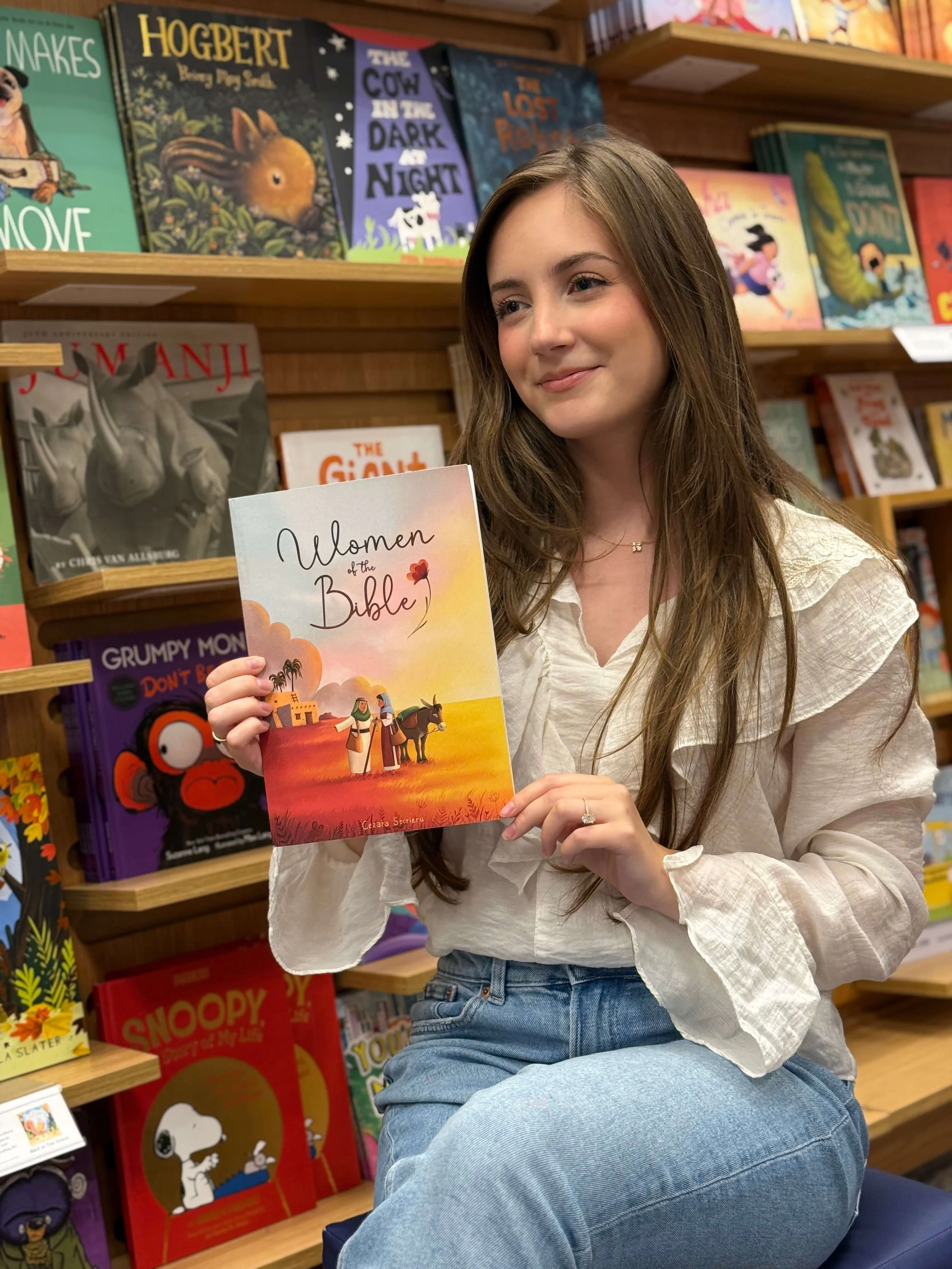 Cezara holding a book titled 'Women of the Bible'. Behind her are shelves filled with children's books.