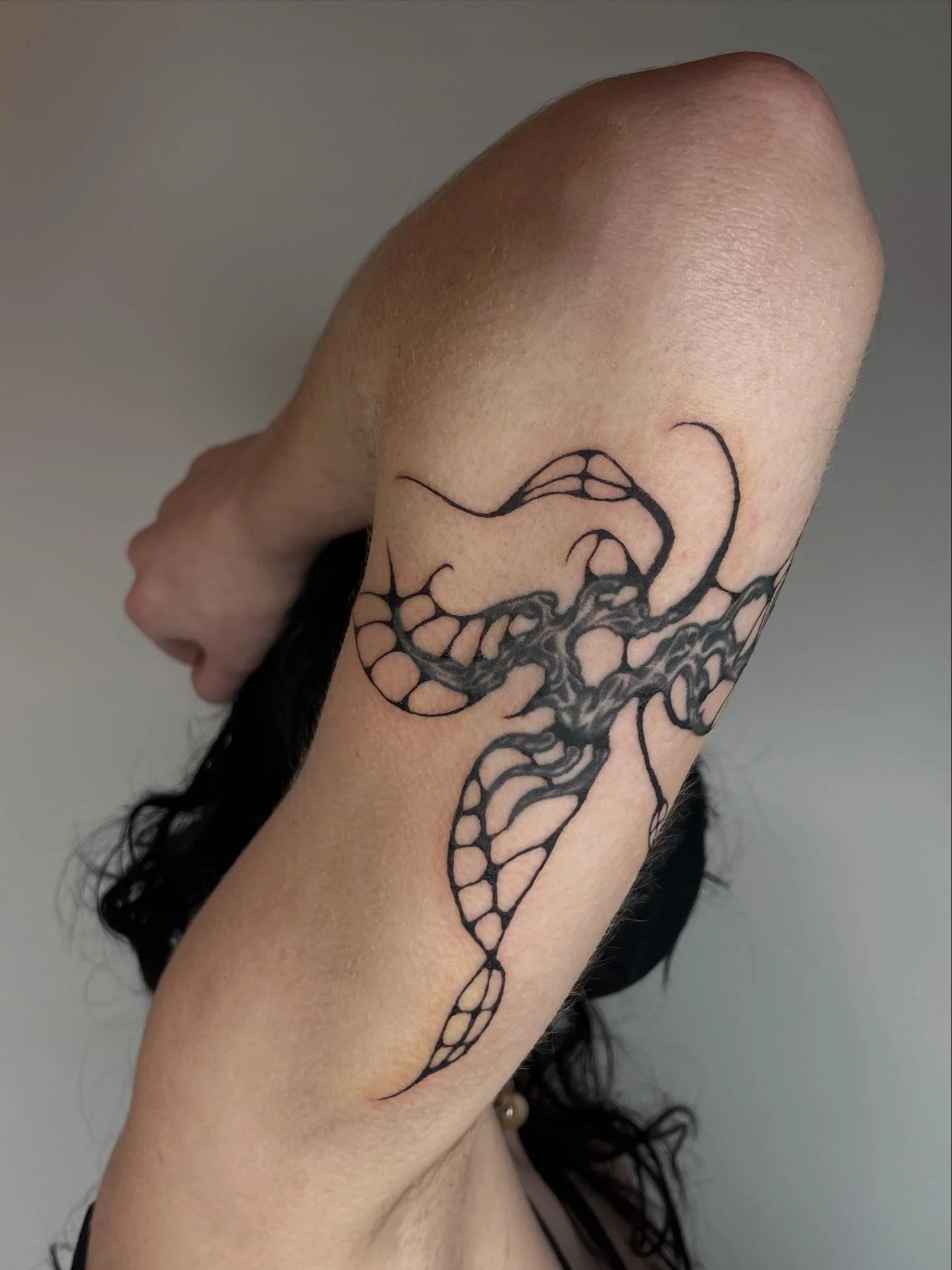 Close-up of a person's arm with a black ink tattoo of a whale and ocean waves.