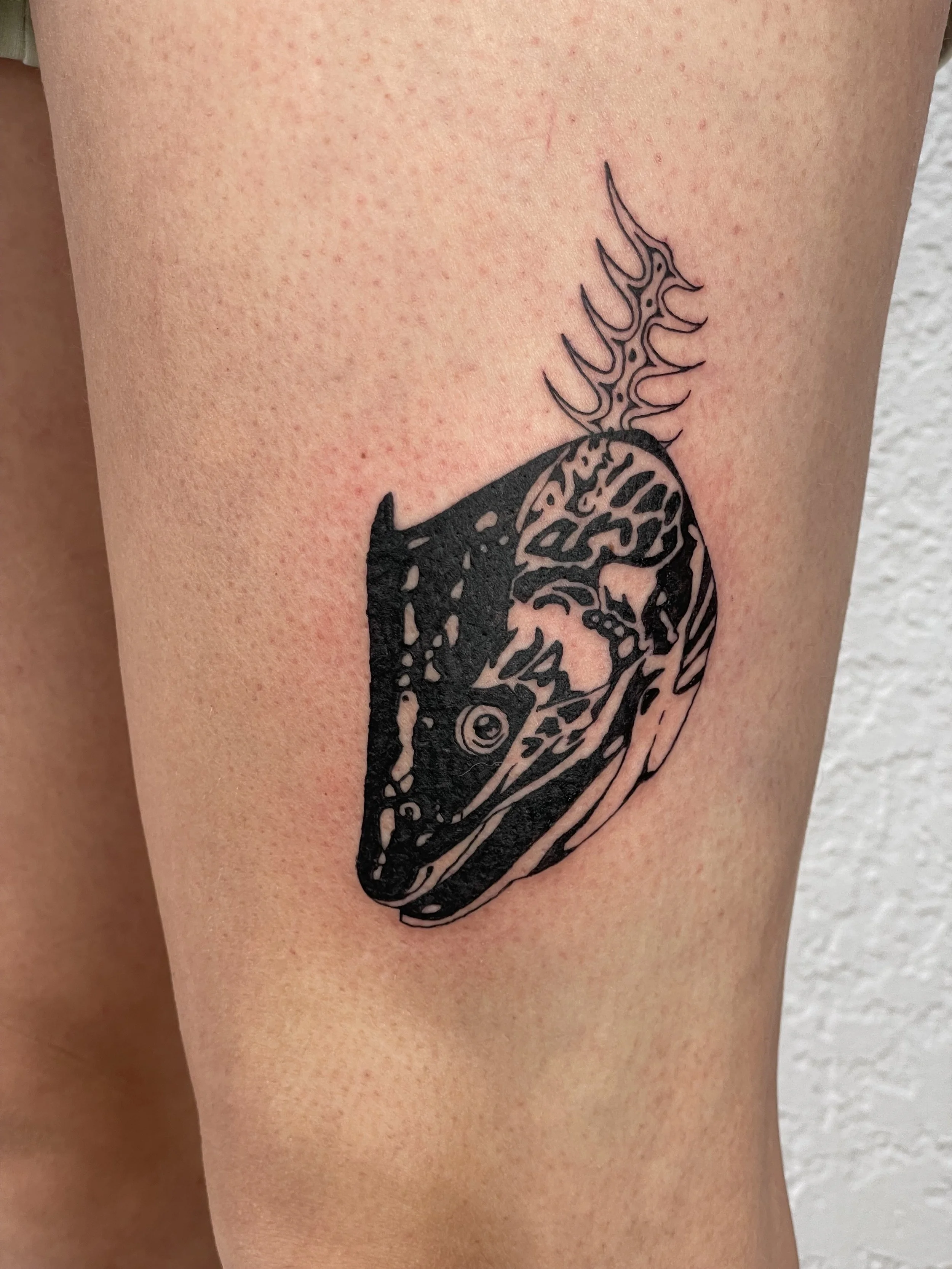 Tattoo of a black and gray salmon head on a person's upper arm.