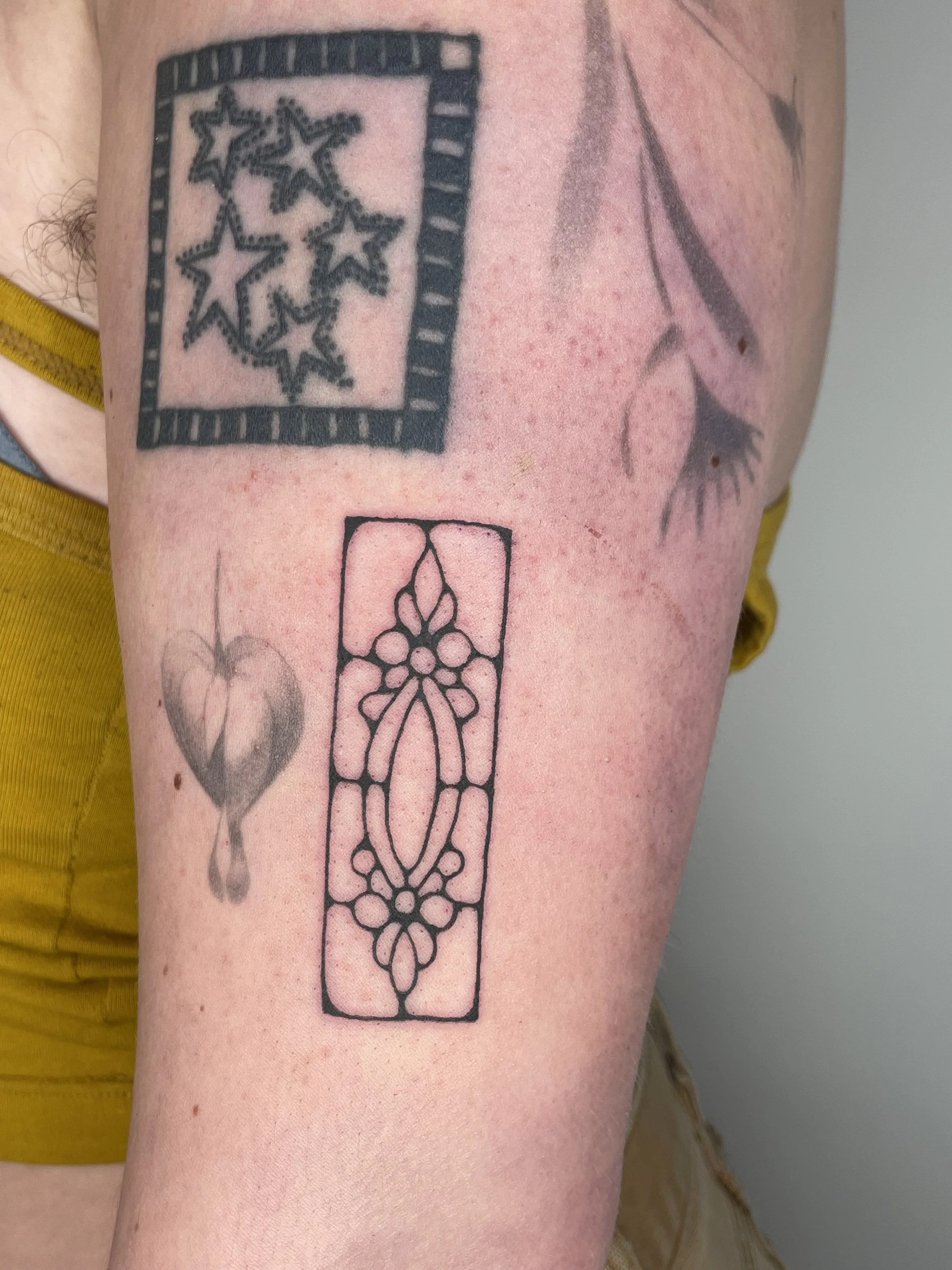 Tattoo of a rectangular frame with a floral pattern inside on a person's arm, alongside a partially visible star and eye tattoo.