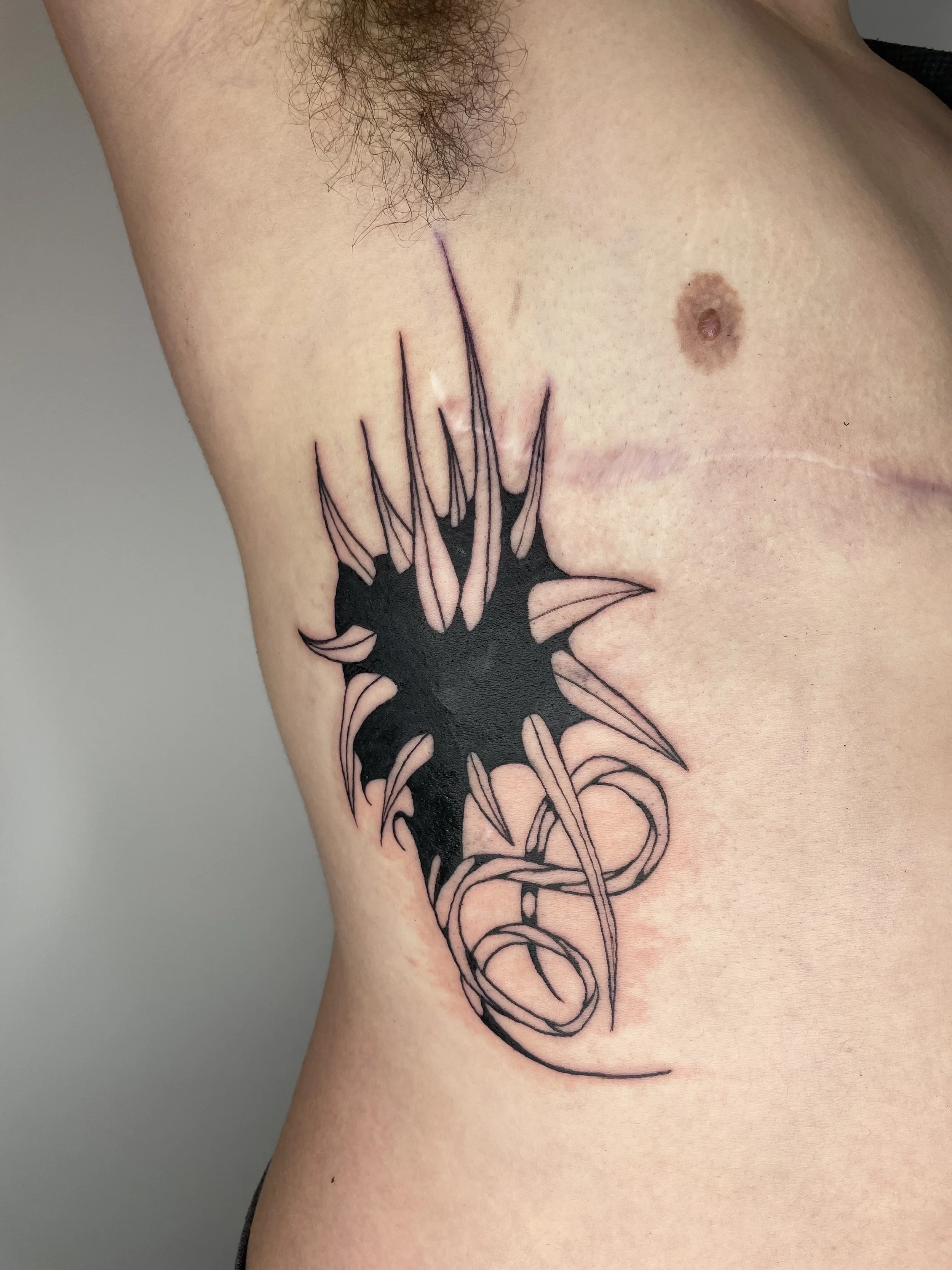 Close-up of a person's side torso with a black and pink tattoo of a bat with wings folded, extending from the ribs to the waist.