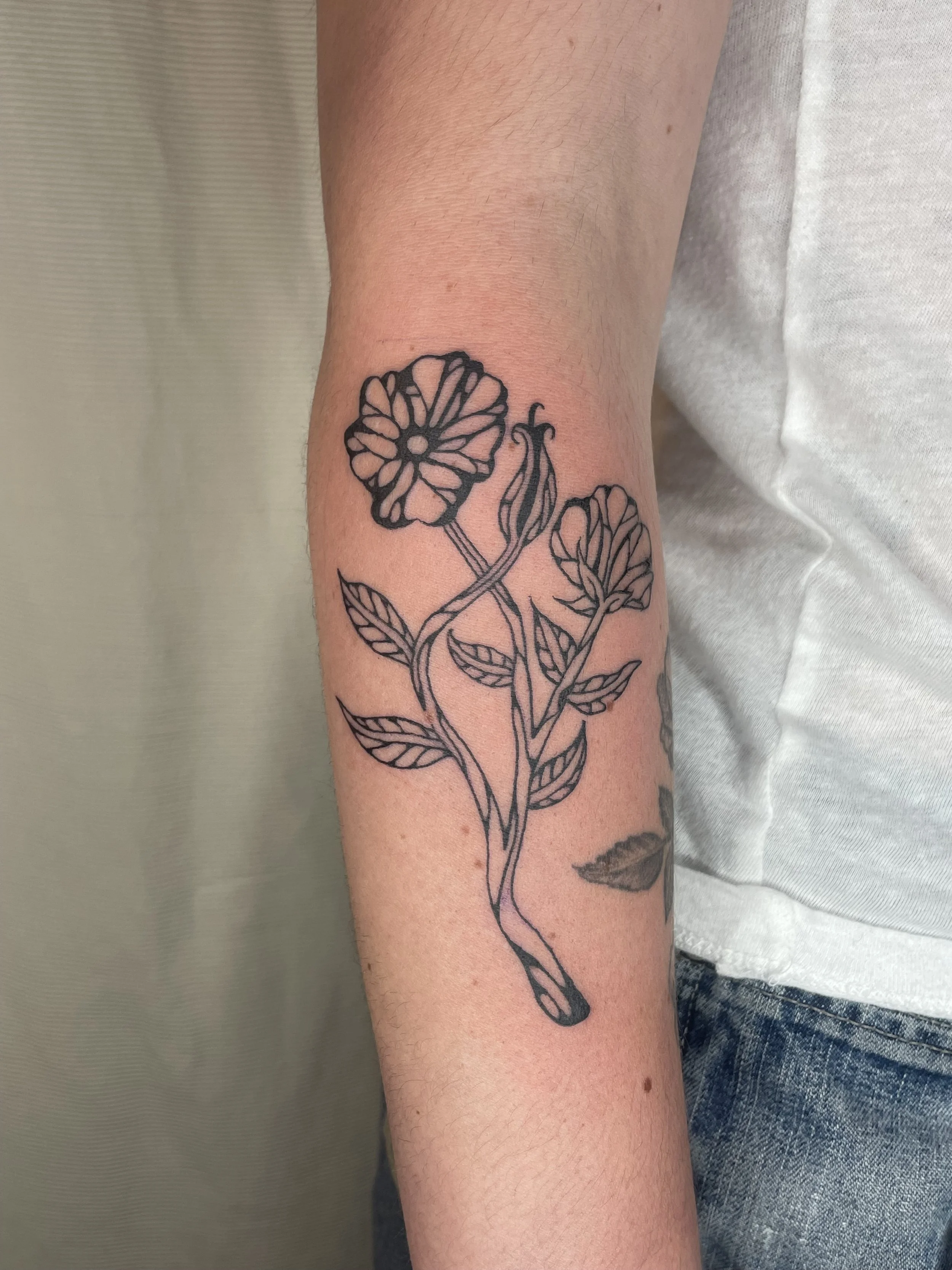 A black outline tattoo of flowers and leaves on a person's forearm.