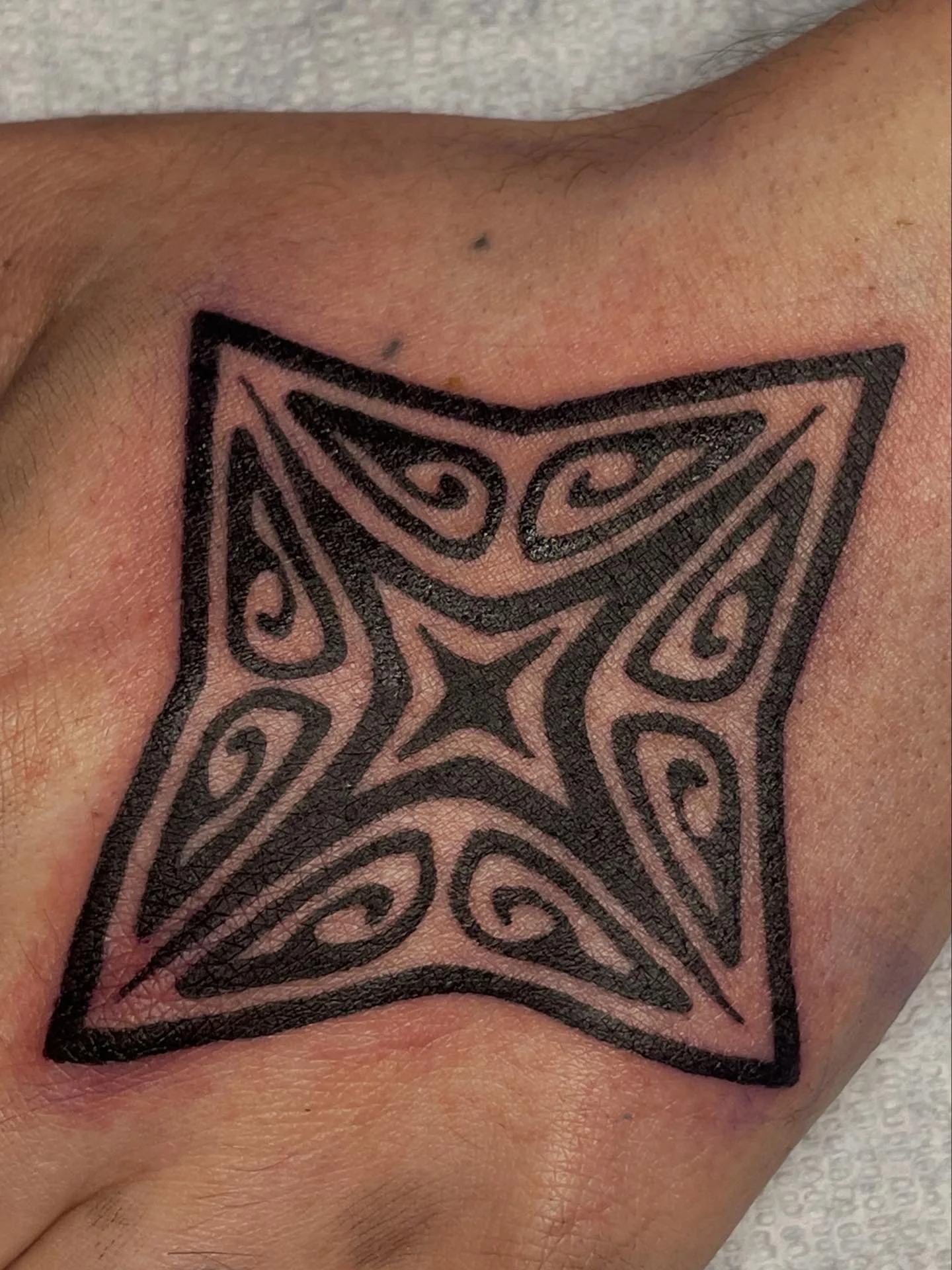 Close-up of a black tattoo design with intricate, swirling patterns on a person's skin.