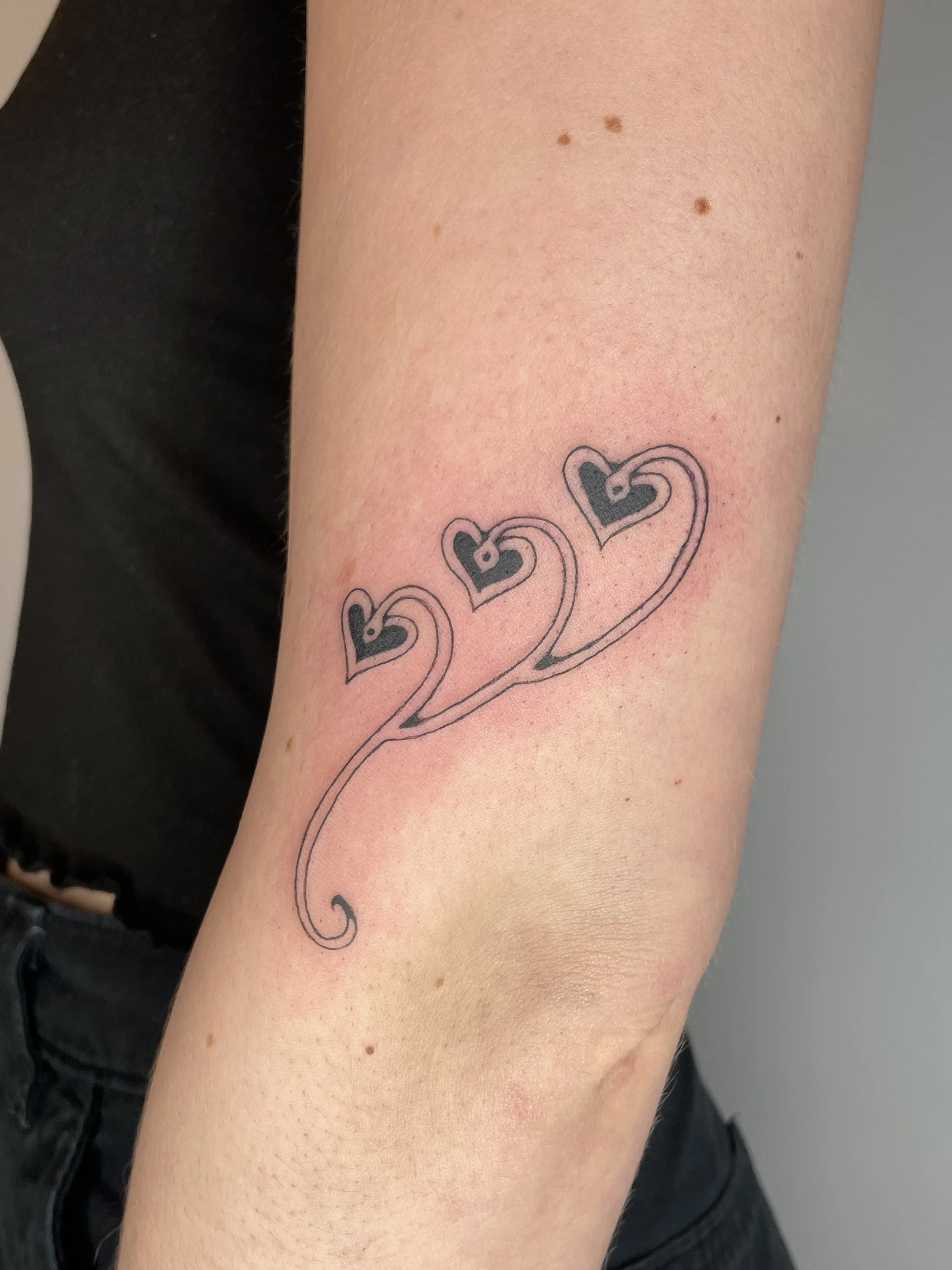 A tattoo of several black hearts connected with curved lines on a person's upper arm.