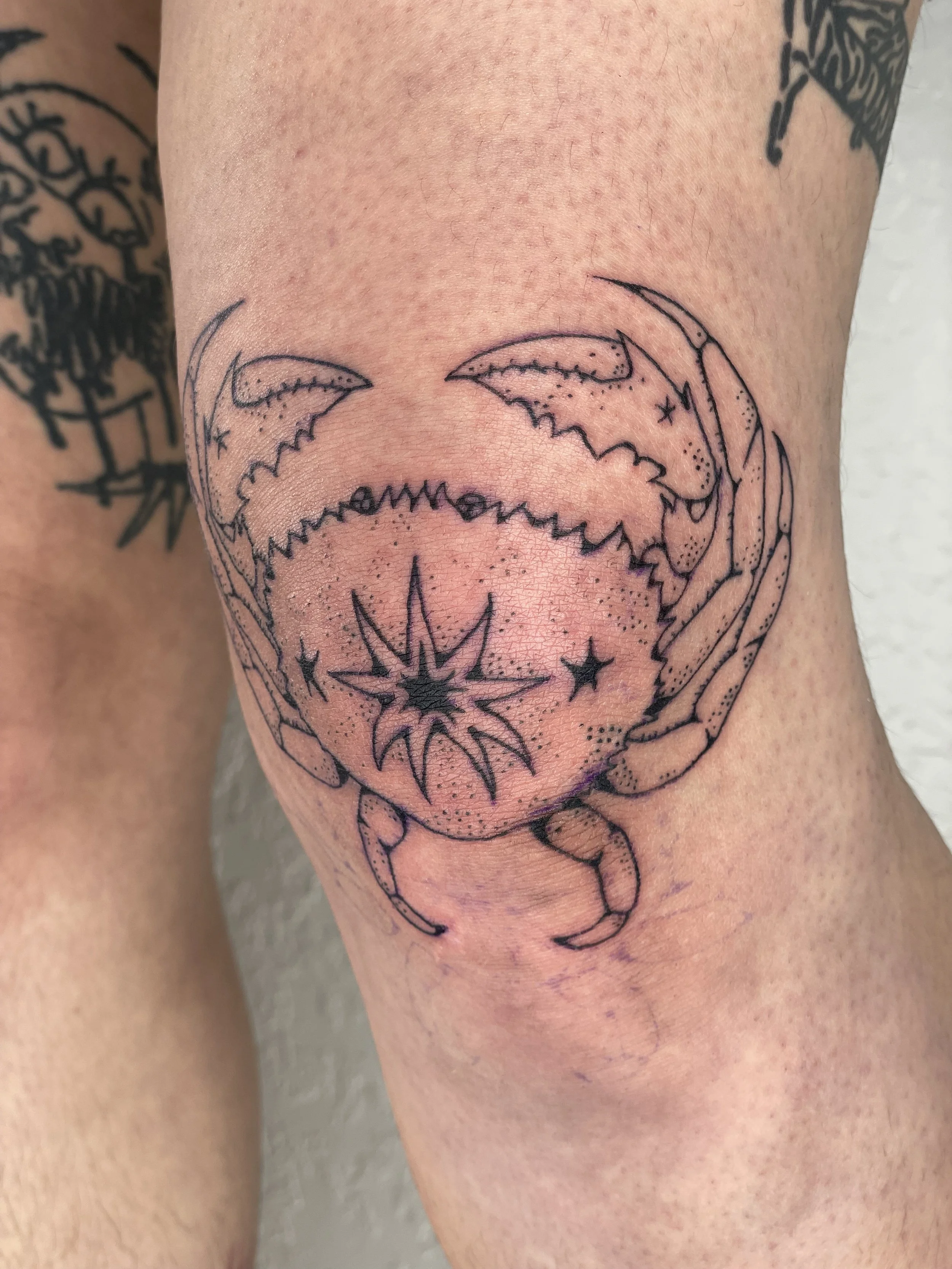 A tattoo of a  crab, stylized with stars , with other tattoos visible nearby.