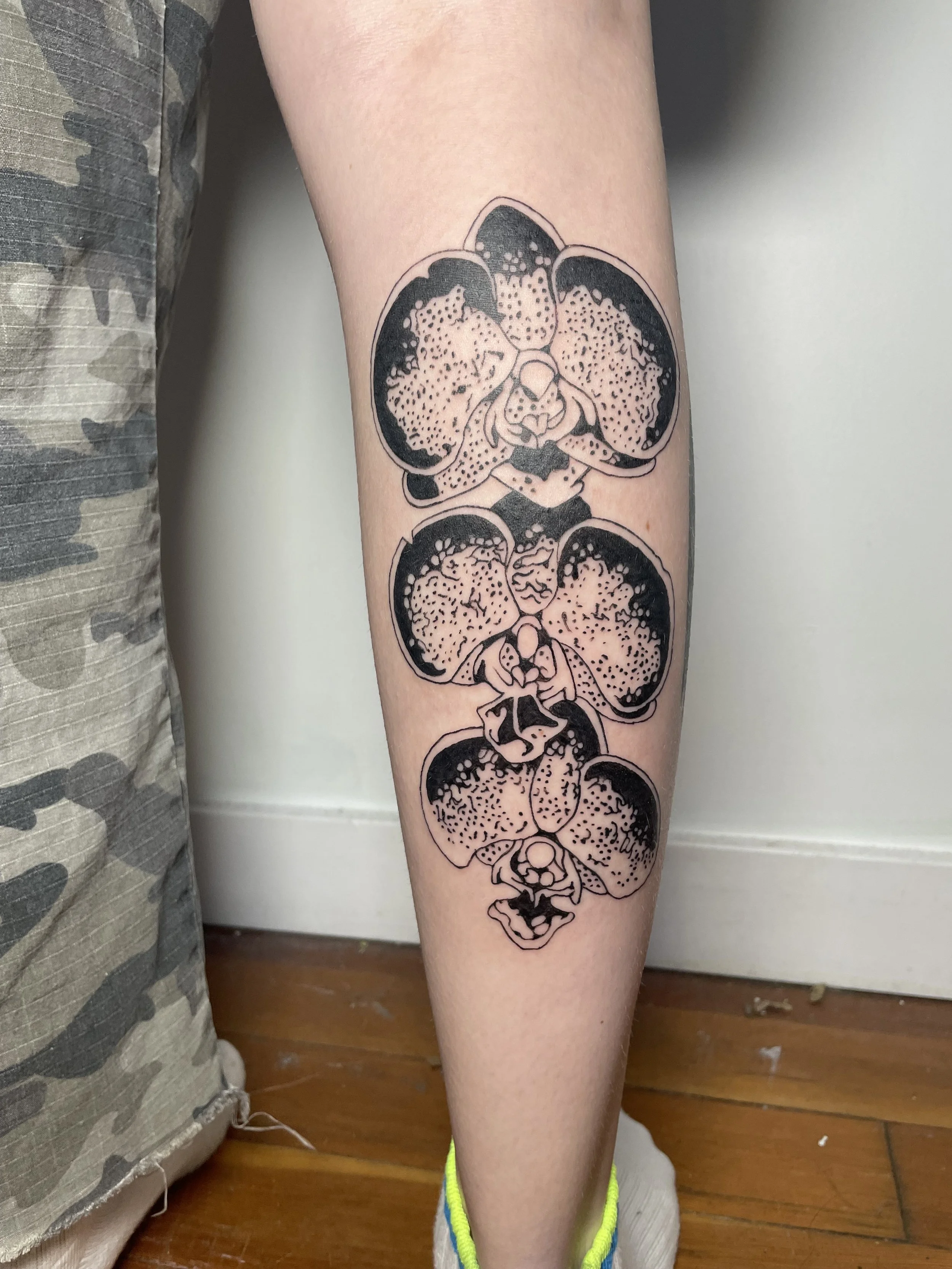 Tattoo of five black and gray orchids on a person's forearm, with detailed petals and shading.