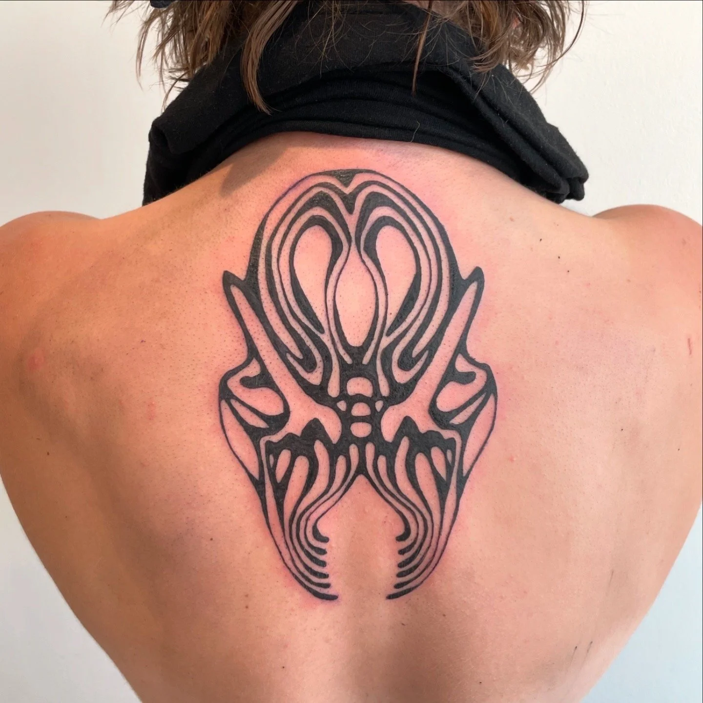 A person's upper back with a large black tribal tattoo design.
