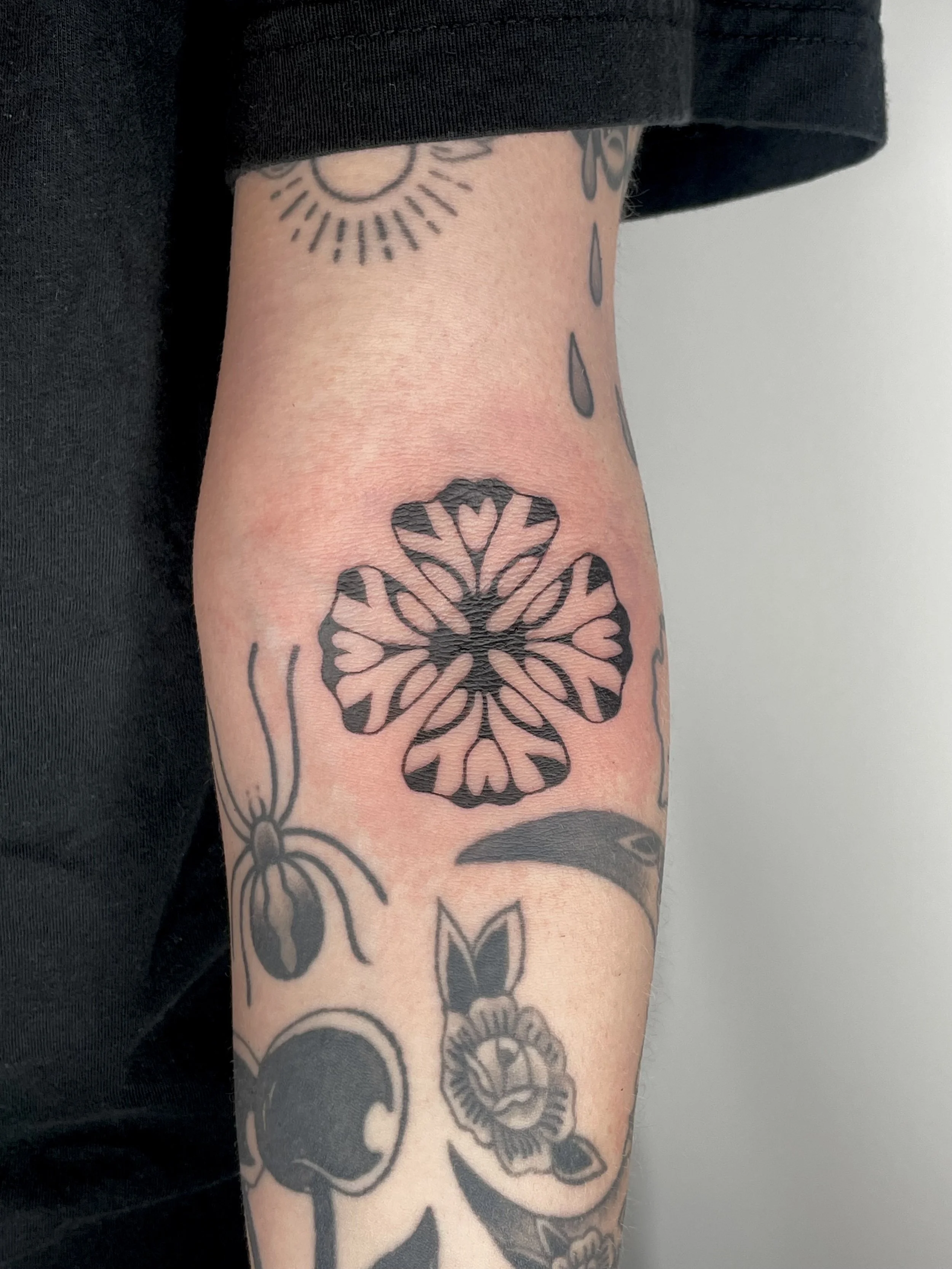 Close-up of a person's arm with multiple black tattoos, including a sunflower, a butterfly, and floral patterns.