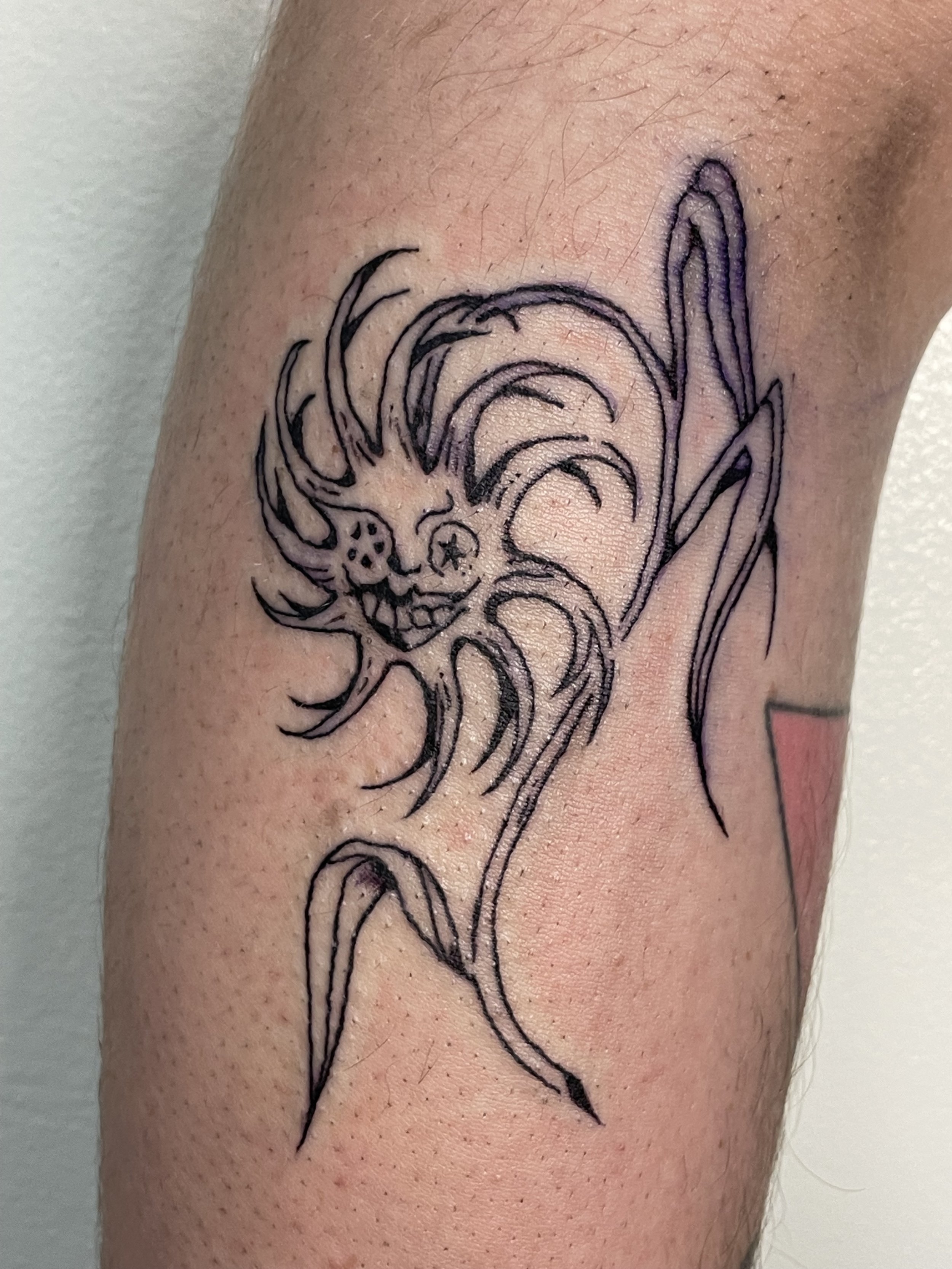 Tattoo of a whimsical face with a small skull and long, flowing hair on a person's arm. flower