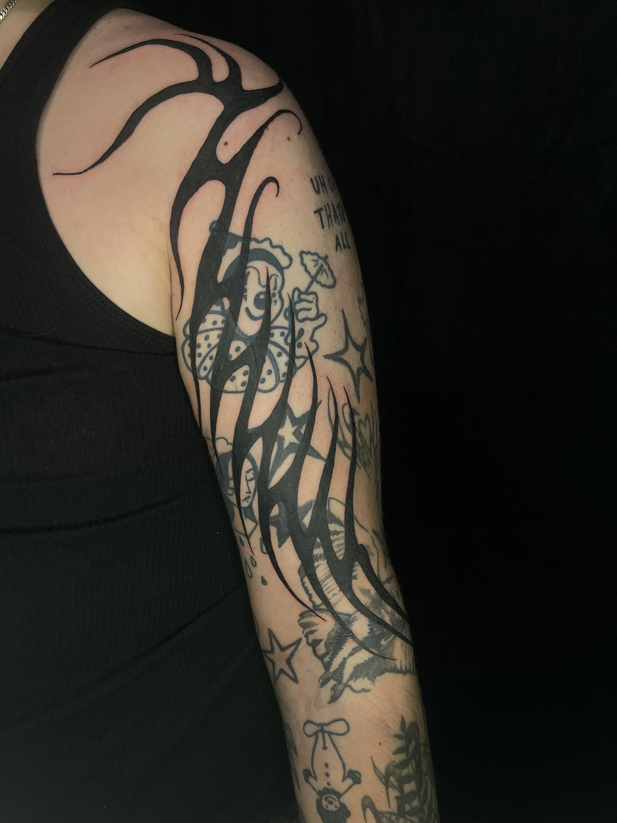 A person's arm with multiple colorful tattoos, including a cartoon character holding an umbrella, stars, and various decorative designs, against a black background. blastover, cover up