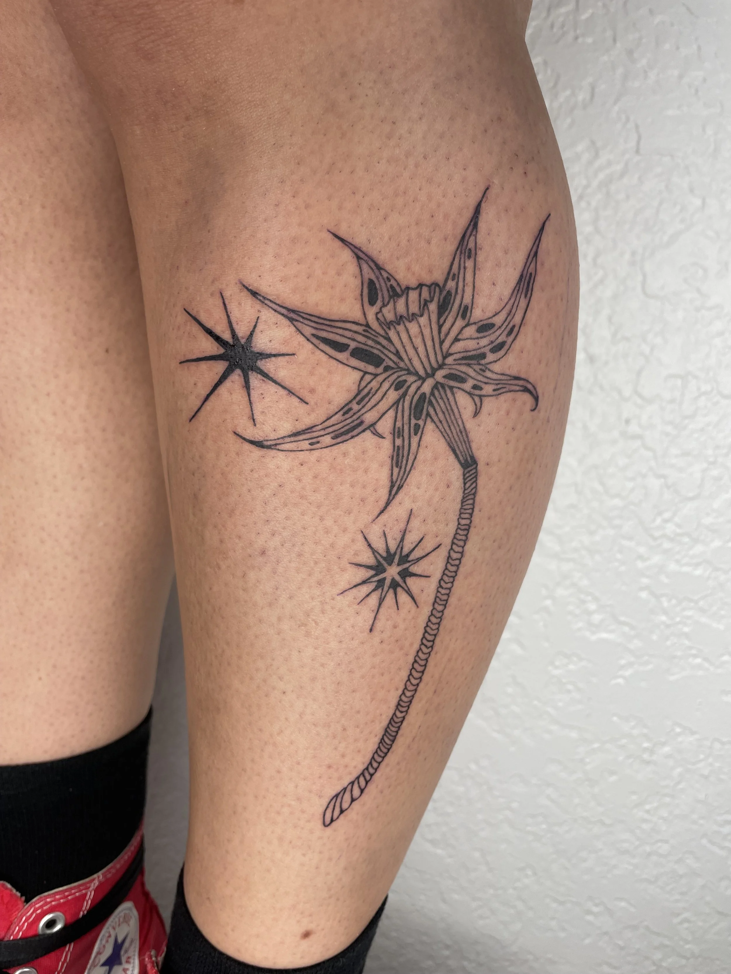 Tattoo of a daffodil styalized, along with two star-like sparkles on a person's upper thigh.