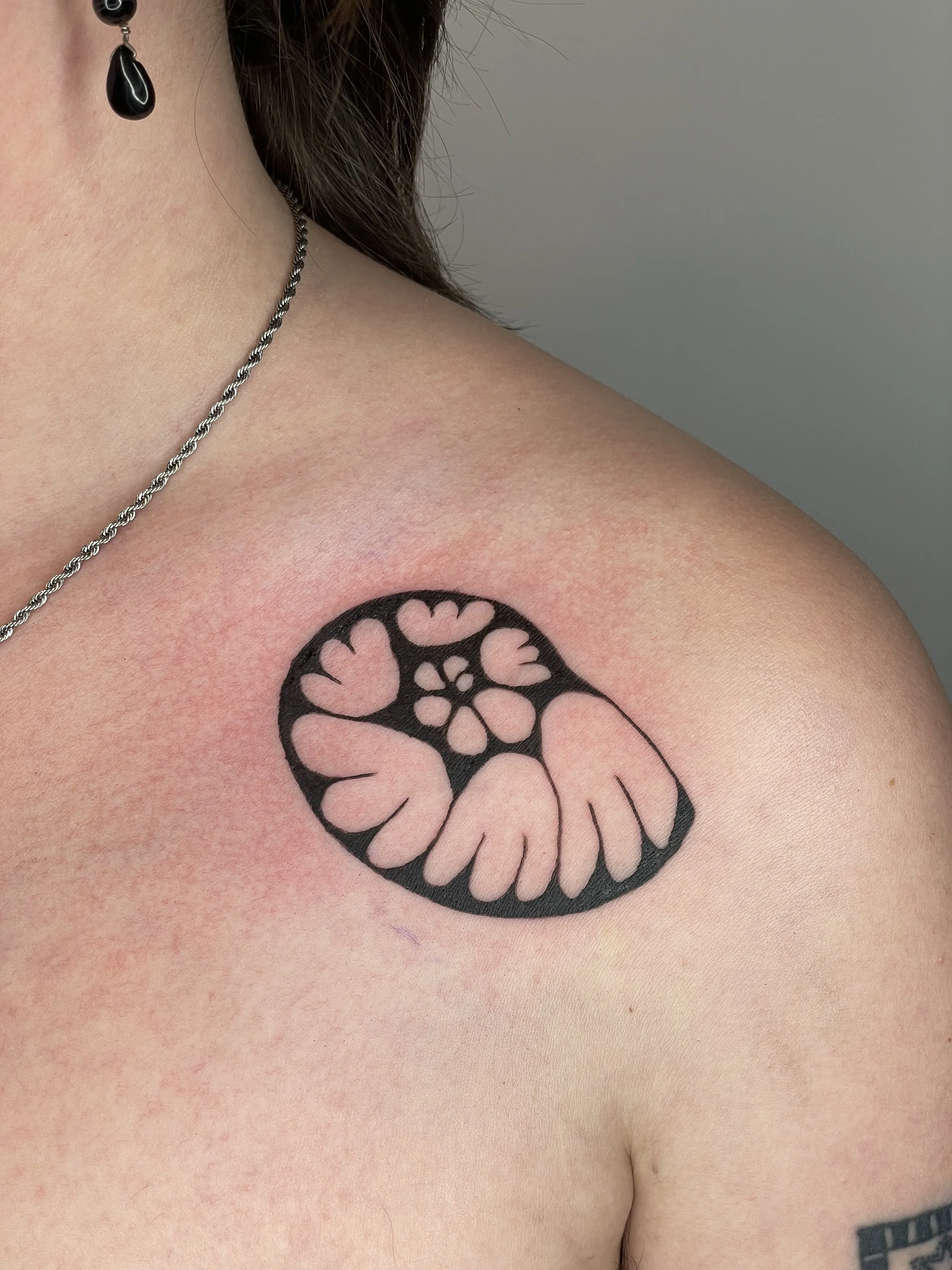 A tattoo of a stylized floral design in black ink on the person's chest near the shoulder.
