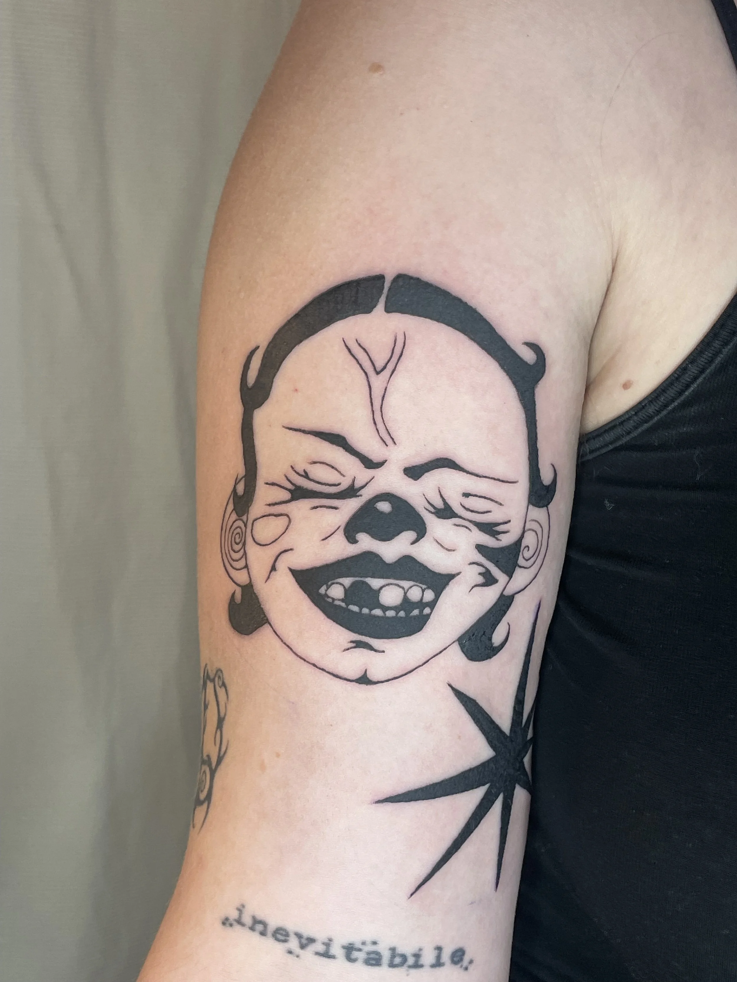 Tattoo of a smiling face with exaggerated features on a person's upper arm.