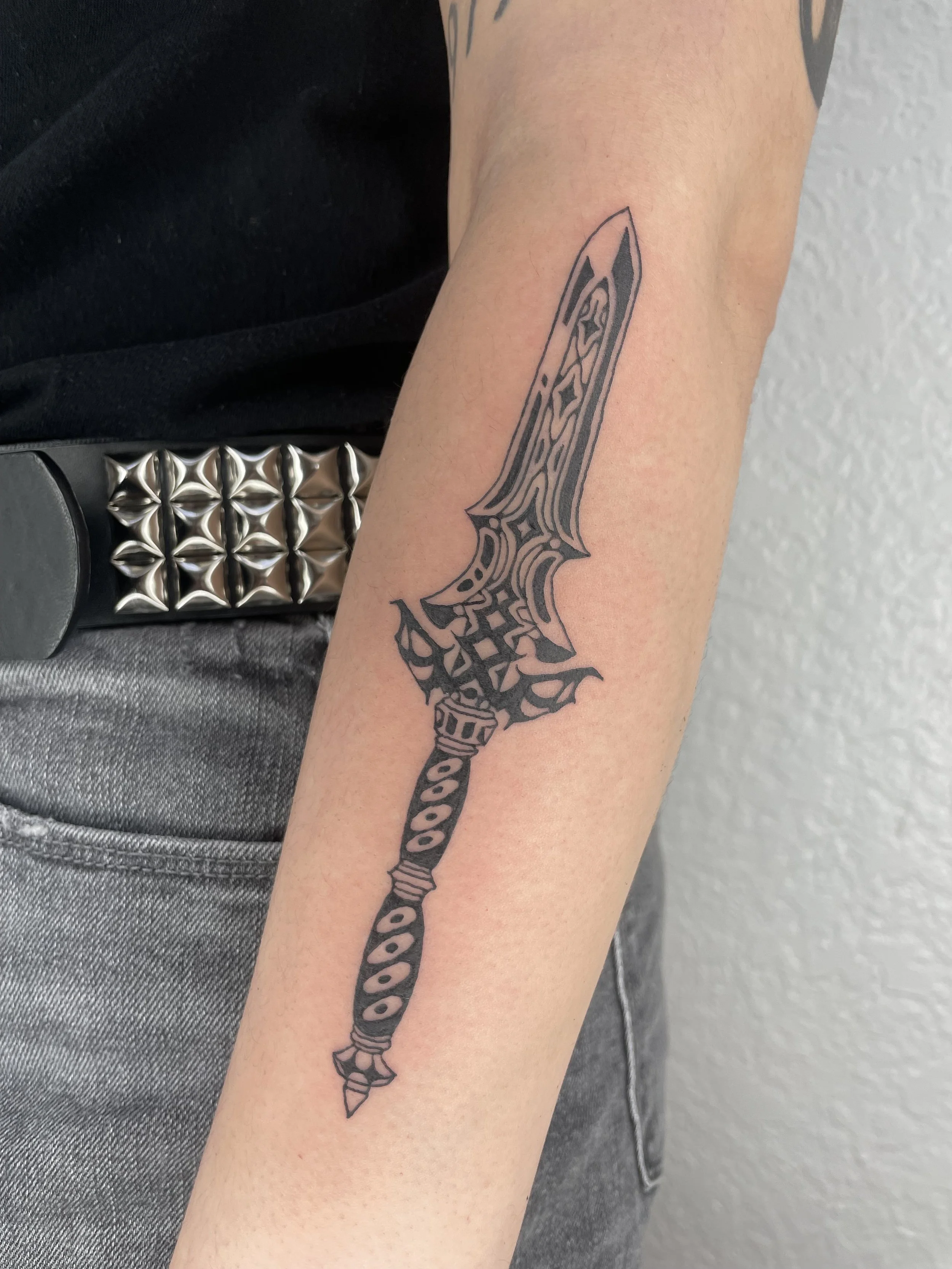A person's forearm with a black tribal-style dagger tattoo. royal claymore, zelda tattoo.