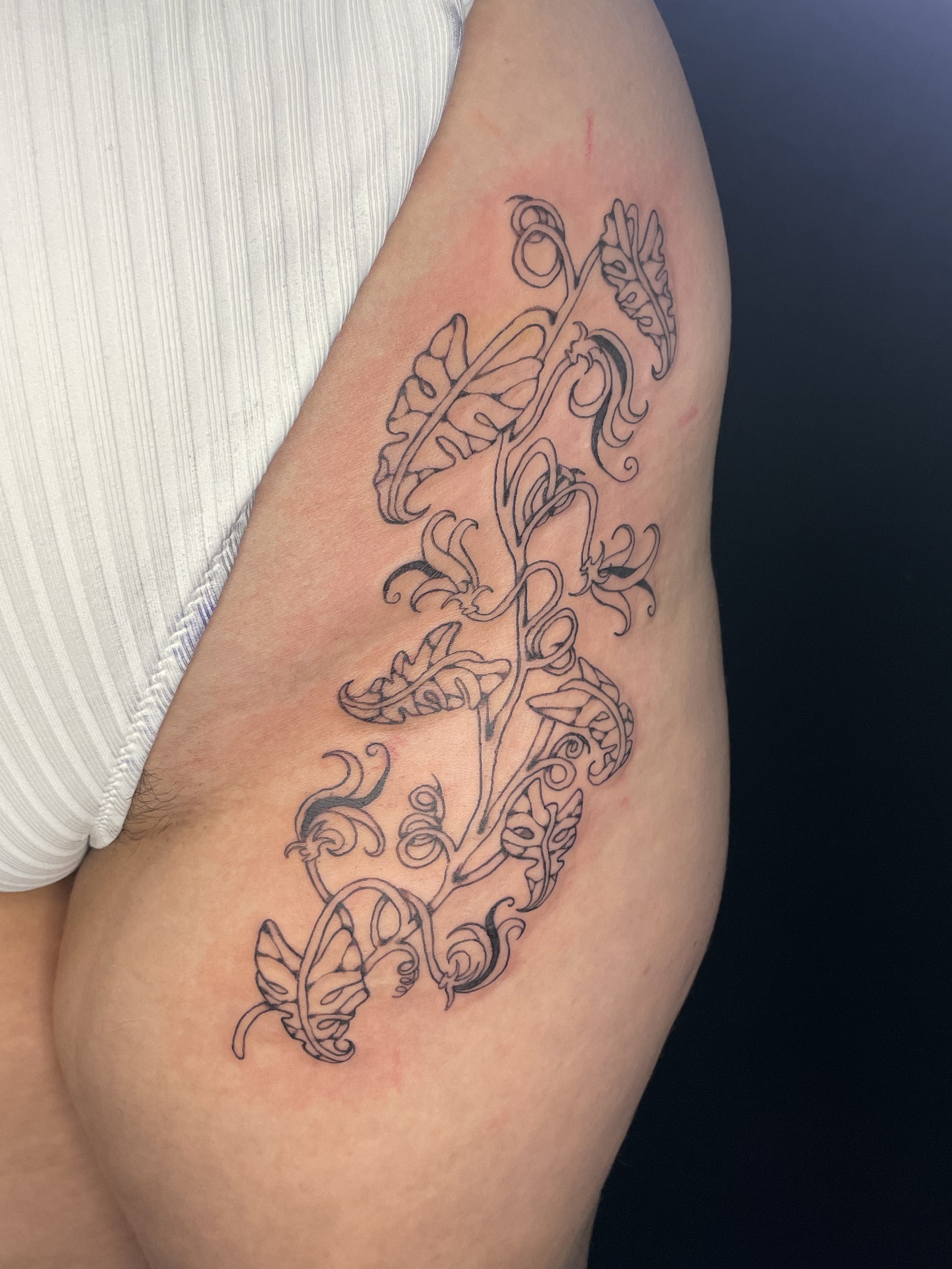 A tattoo of intricate line art floral and leafy design running down a person's upper arm.